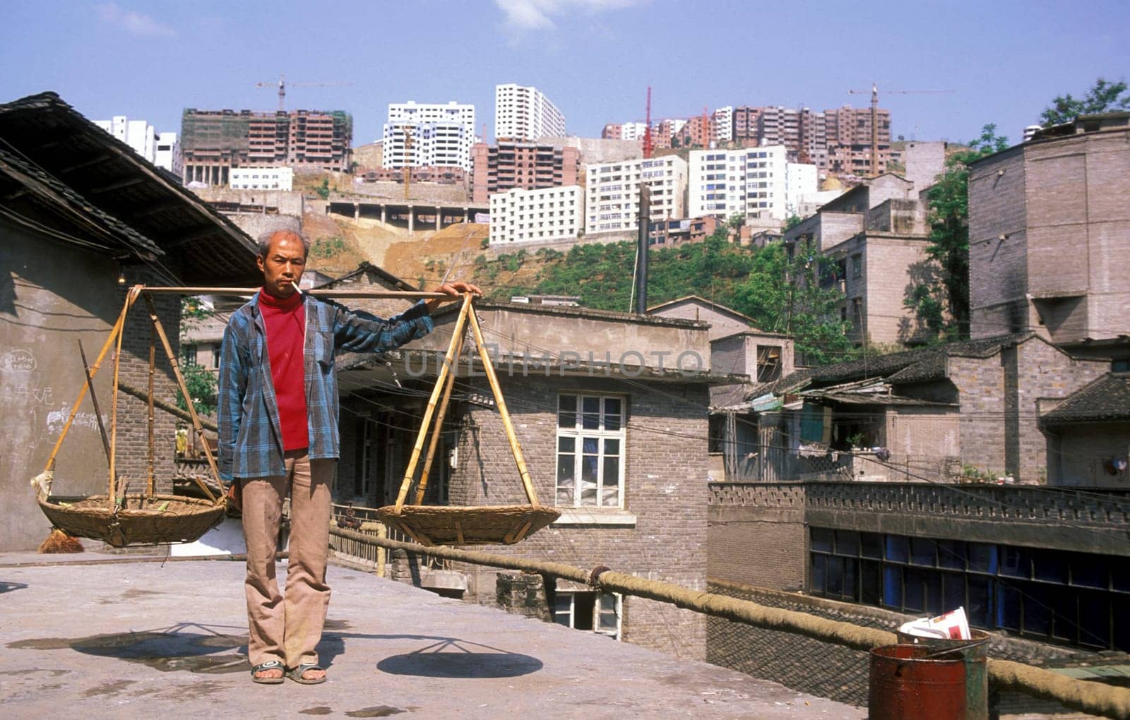 a men in the old city with the new city in the back in the city of wushan on the yangzee river near the three gorges valley up of the three gorges dam project in the province of hubei in china.