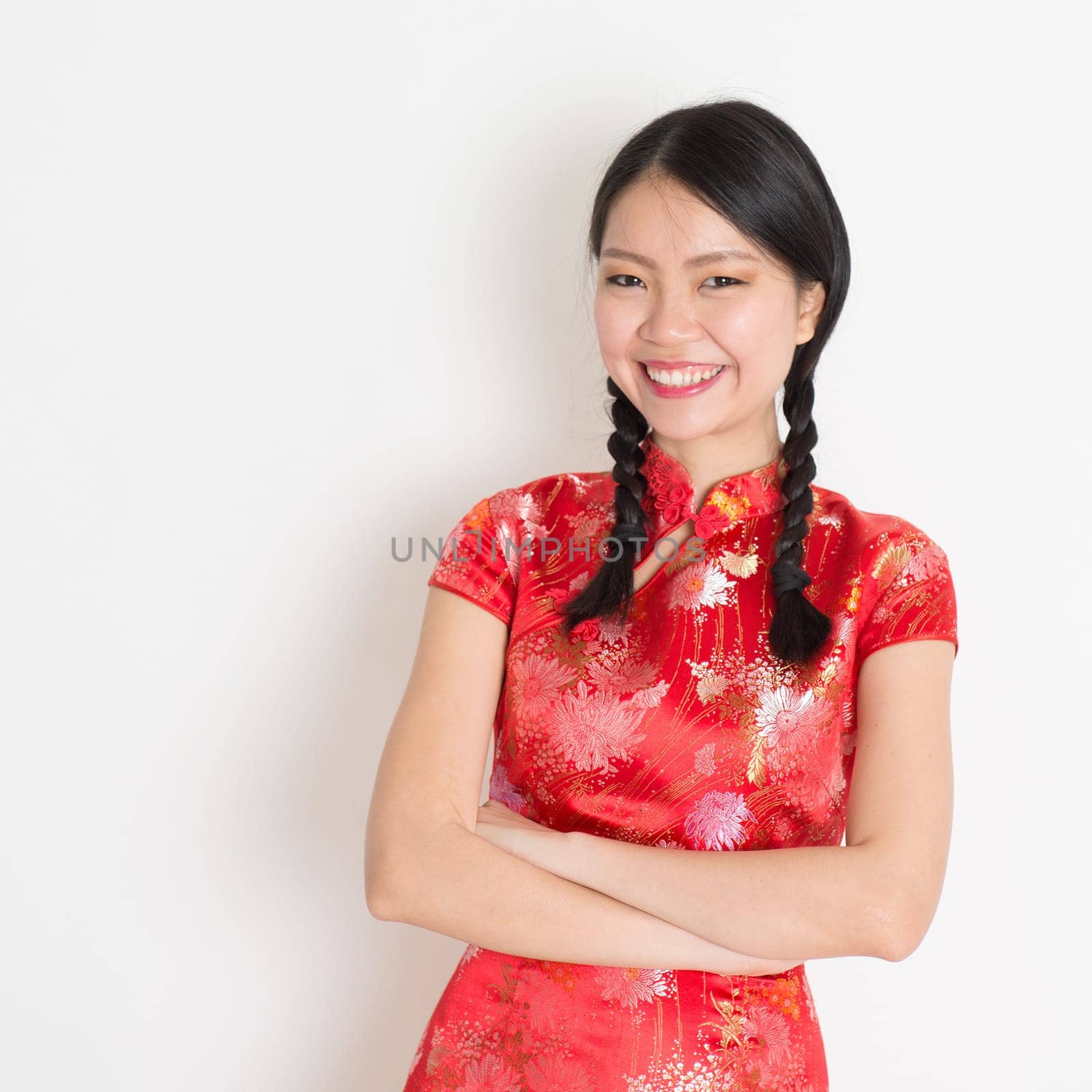 Portrait of Asian Chinese girl smiling, in traditional red qipao standing on plain background.