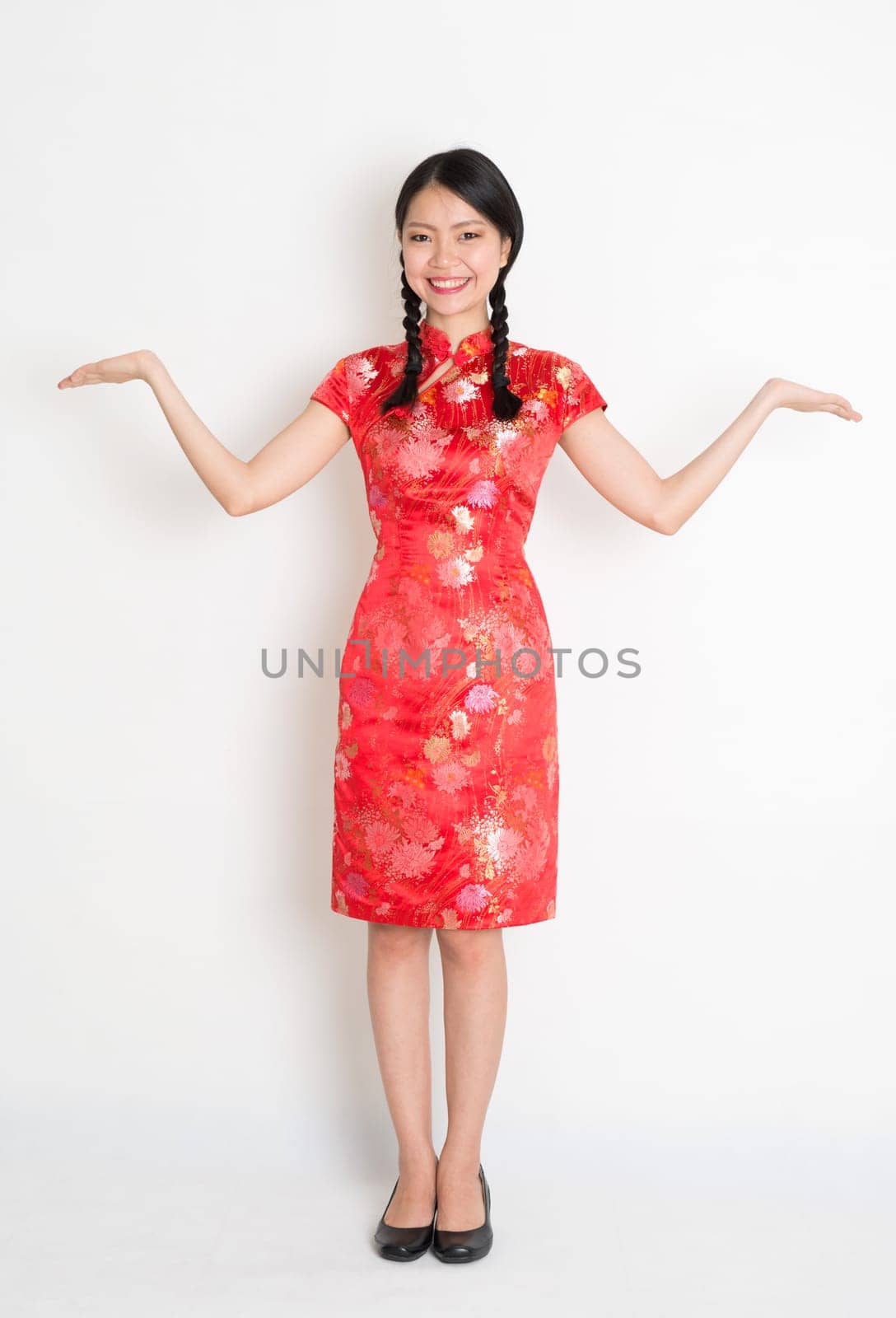 Portrait of full length Asian Chinese girl open palms with copy space, showing somethind, in traditional red cheongsam standing on plain background.