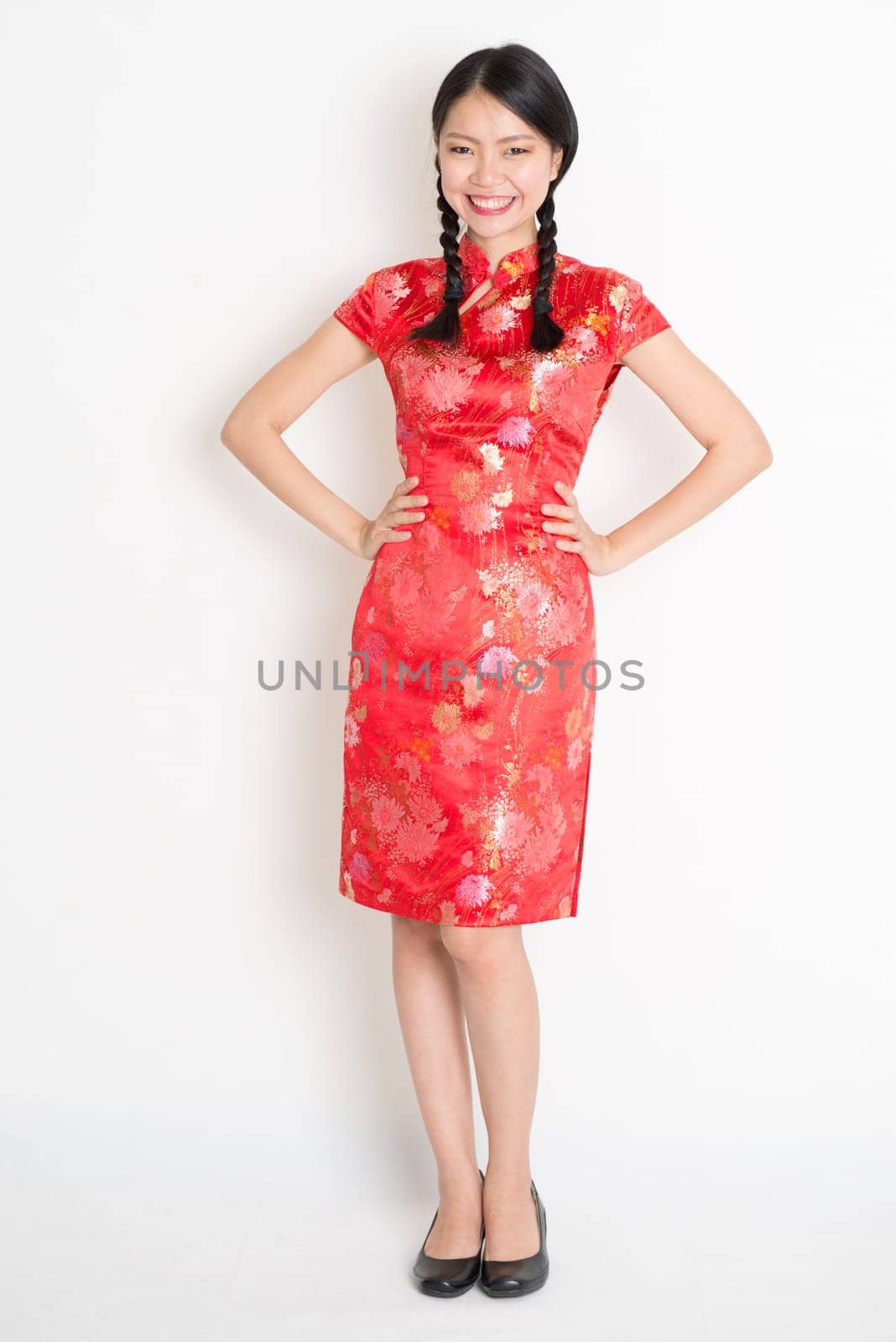 Portrait of full length Asian Chinese girl, in traditional red cheongsam standing on plain background.