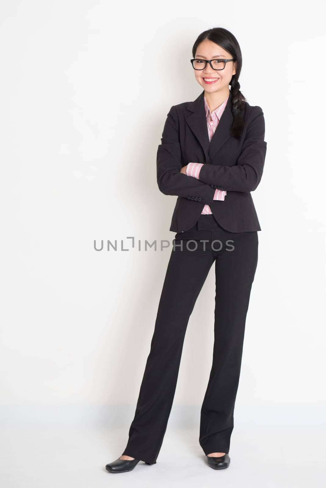 Full body Asian business woman smiling and standing on plain background.