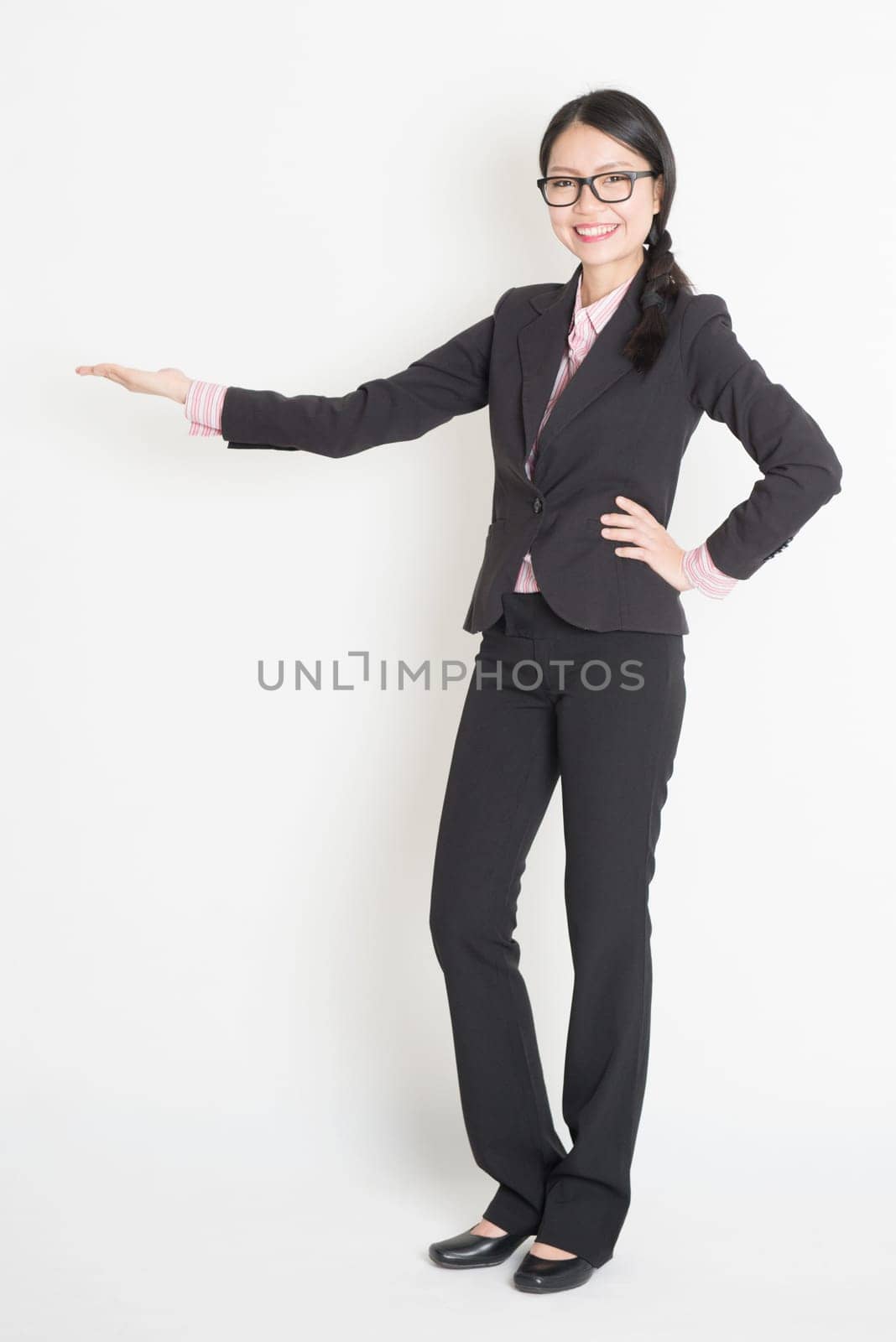 Full body Asian business woman showing copy space, hand holding something, standing on plain background.