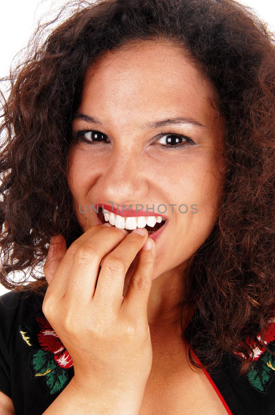 A closeup of the face of a young woman with curly brunette hair biting.her finger nail..