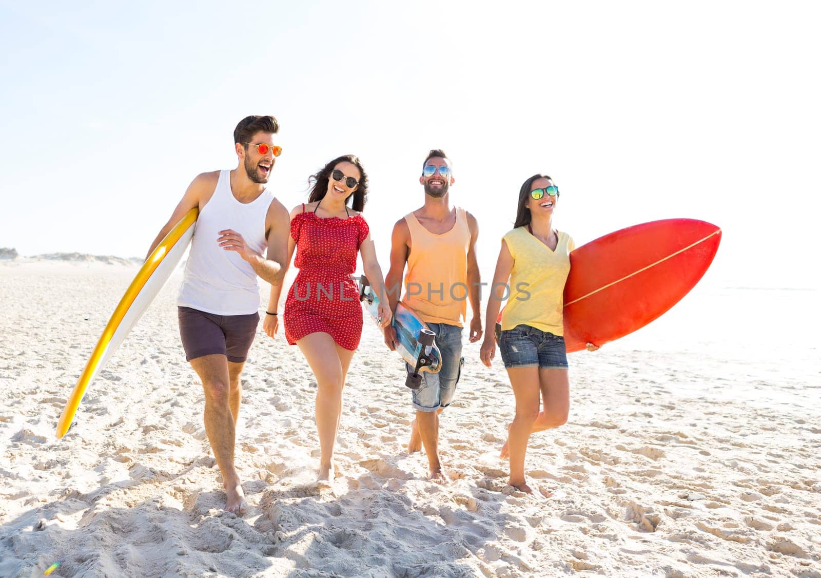 Group of friends walking together at the beach and holding surfboards