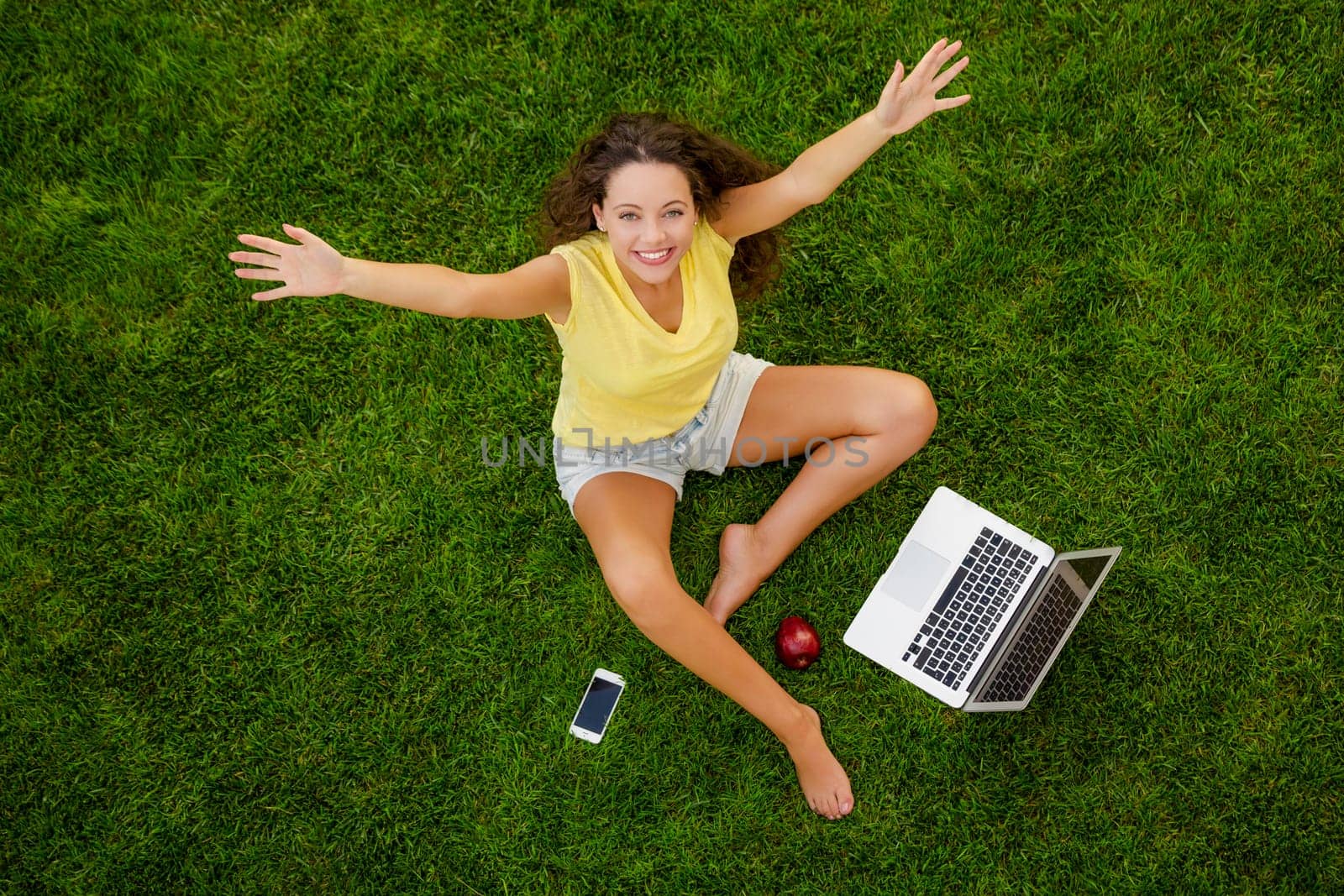 Beautiful young woman lying on the grass and working with a laptop