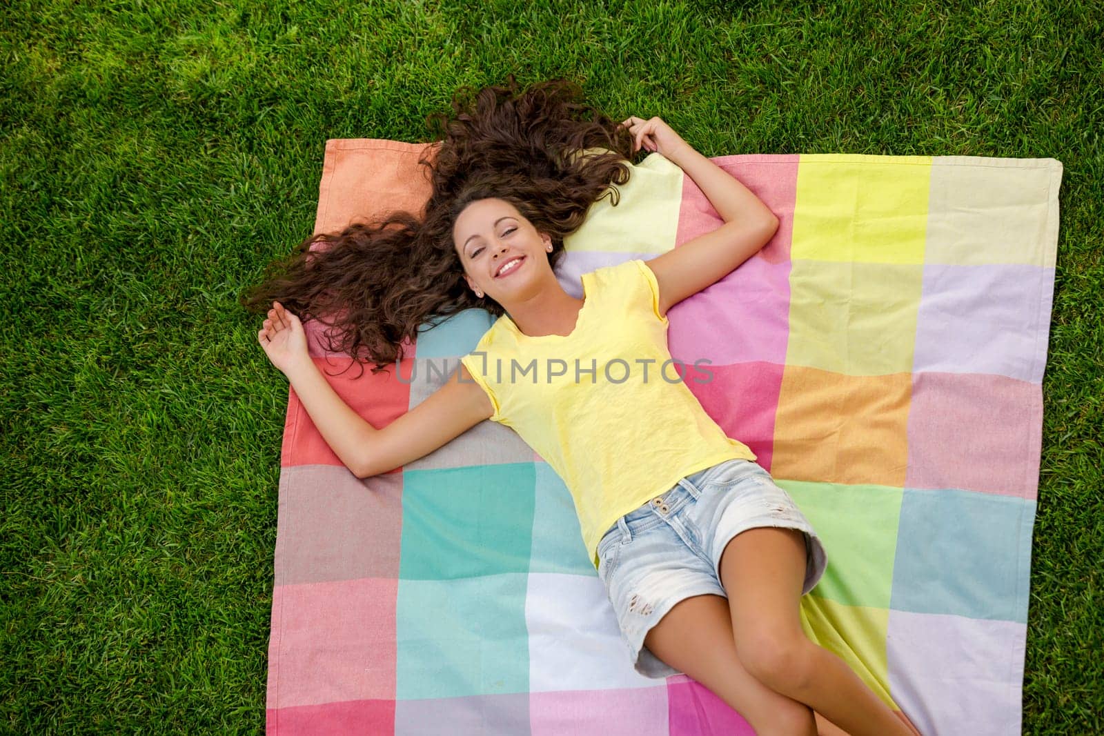 Happy young woman sitting on a blanket with arms stretched
