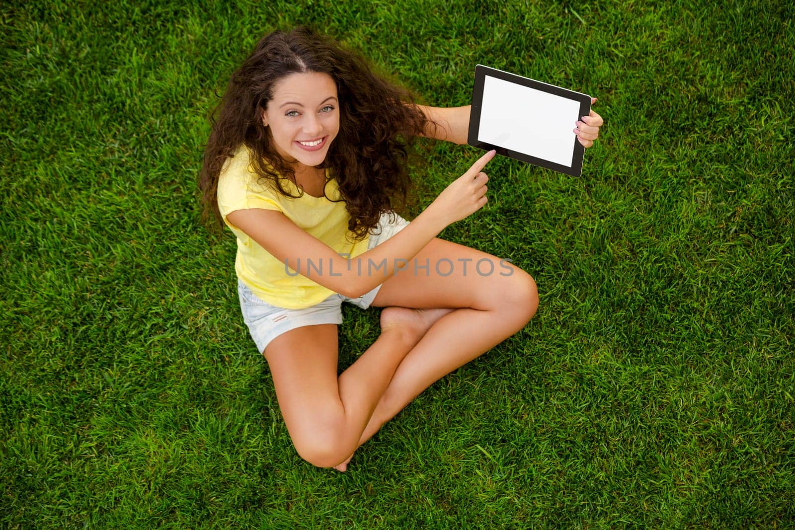 Beautiful young woman sitting on the grass and holding a tablet