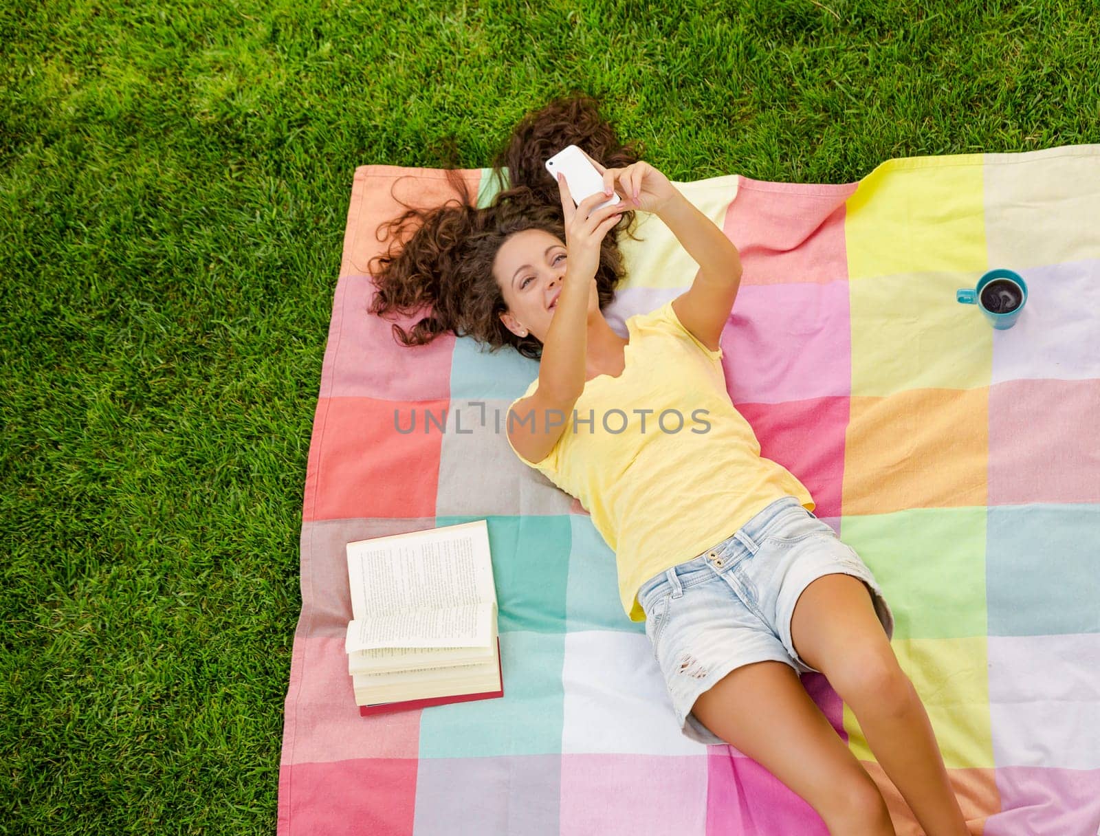 Happy young woman sitting on a blanket with arms stretched