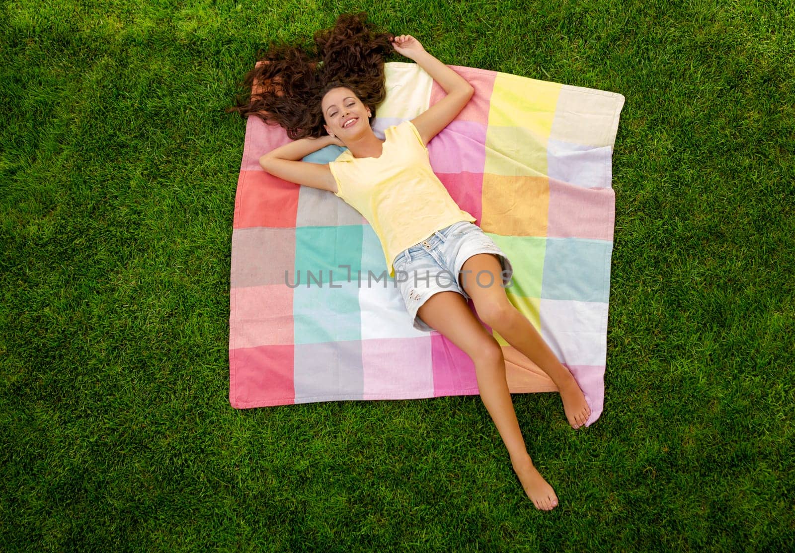 Happy young woman sitting on a blanket with arms stretched
