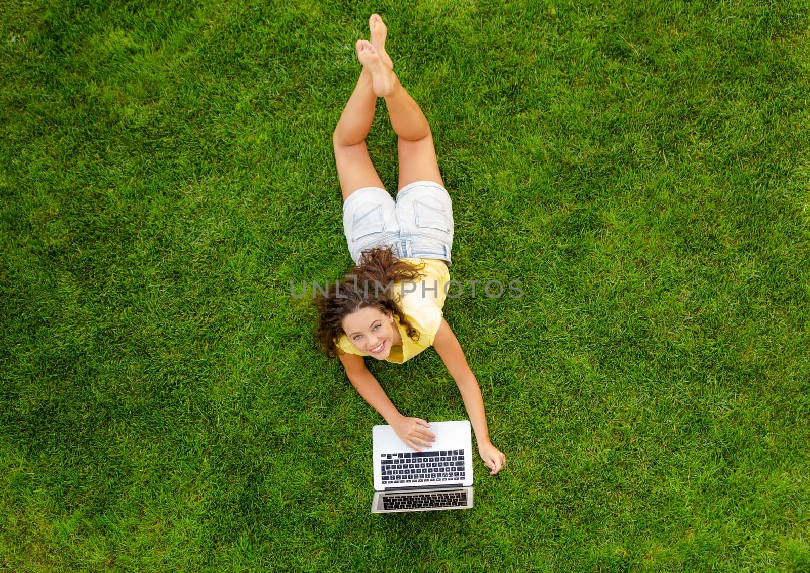 Beautiful young woman lying on the grass and working with a laptop