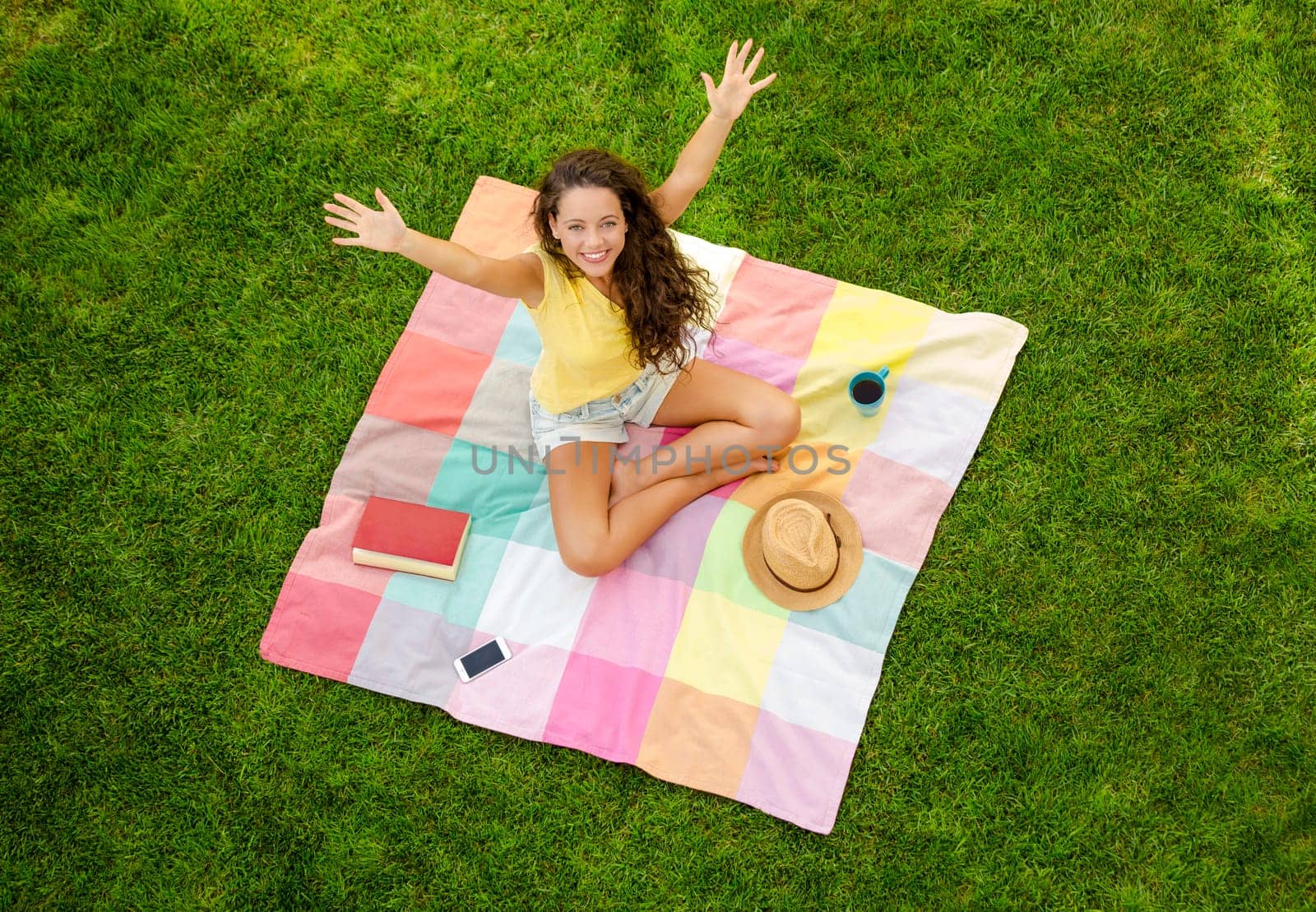 Happy young woman sitting on a blanket with arms stretched