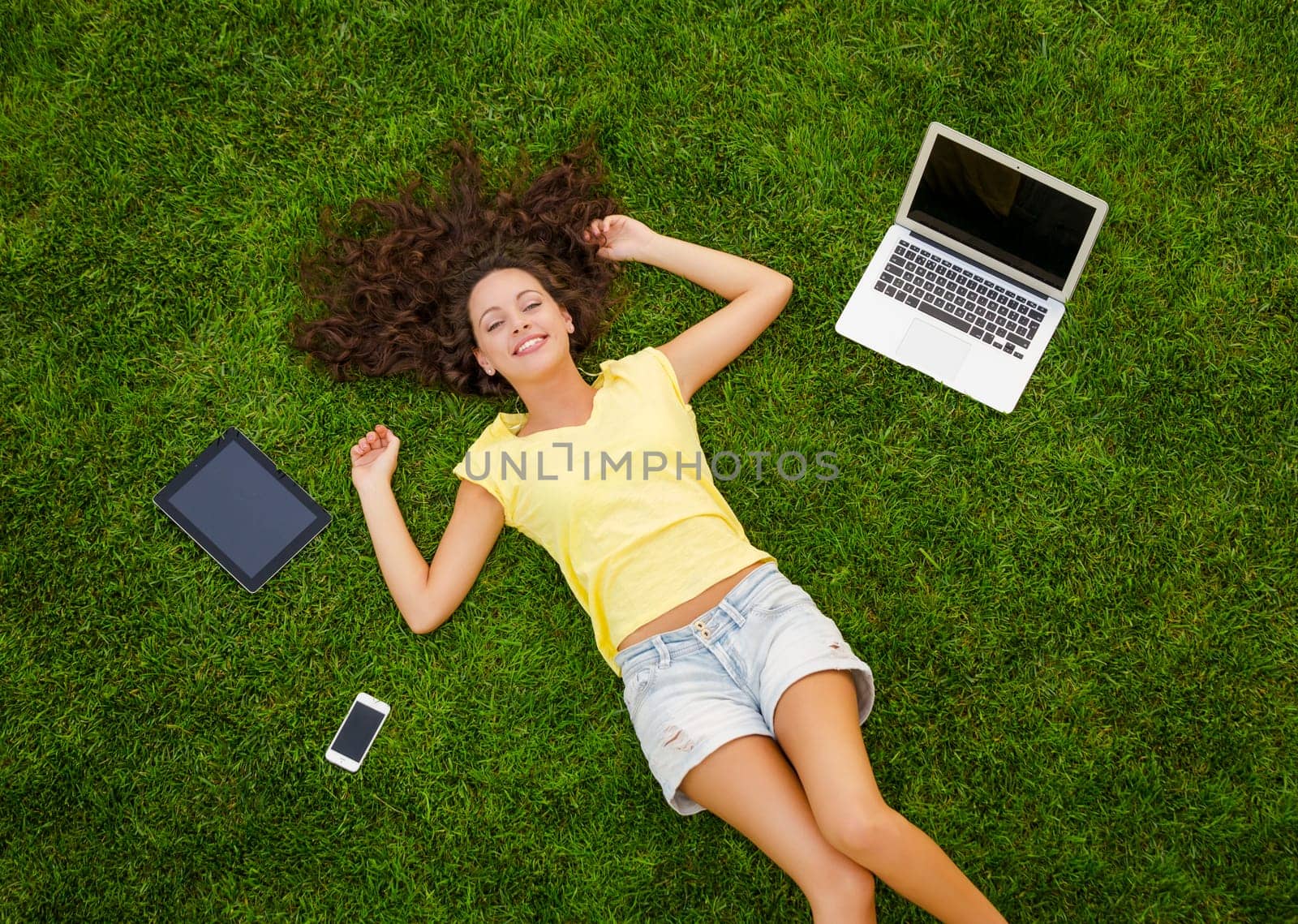 Beautiful young woman lying on the grass and working with a laptop