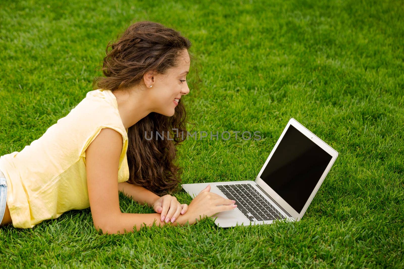 Beautiful young woman lying on the grass and working with a laptop