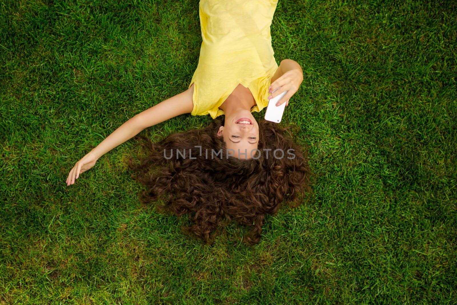 Smiling young woman lying on the grass and making a selfie