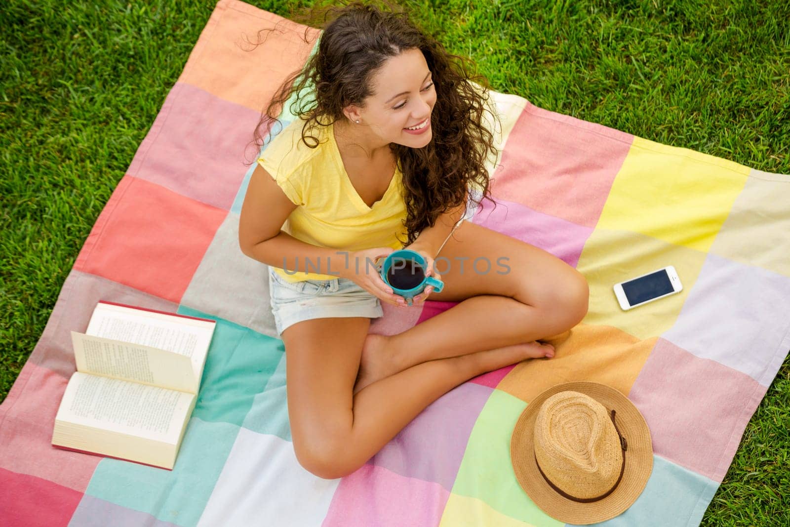 Happy young woman sitting on a blanket with arms stretched