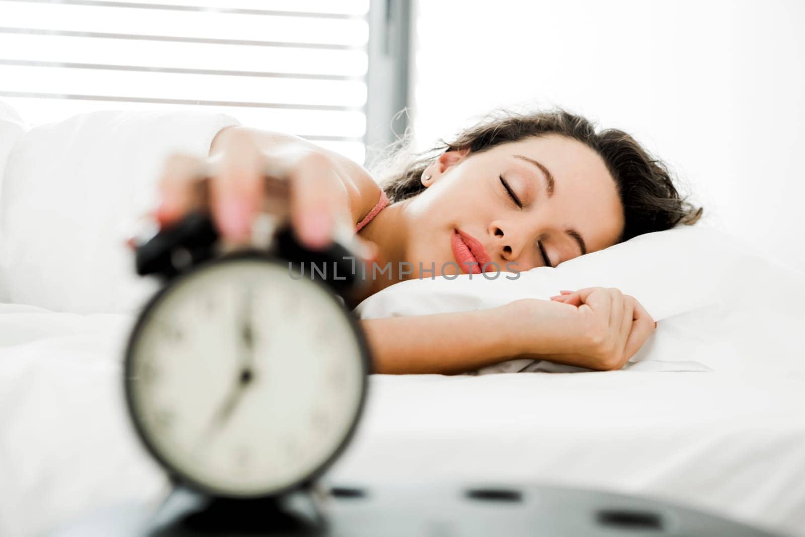 Beautiful young woman waking up with the alarm clock