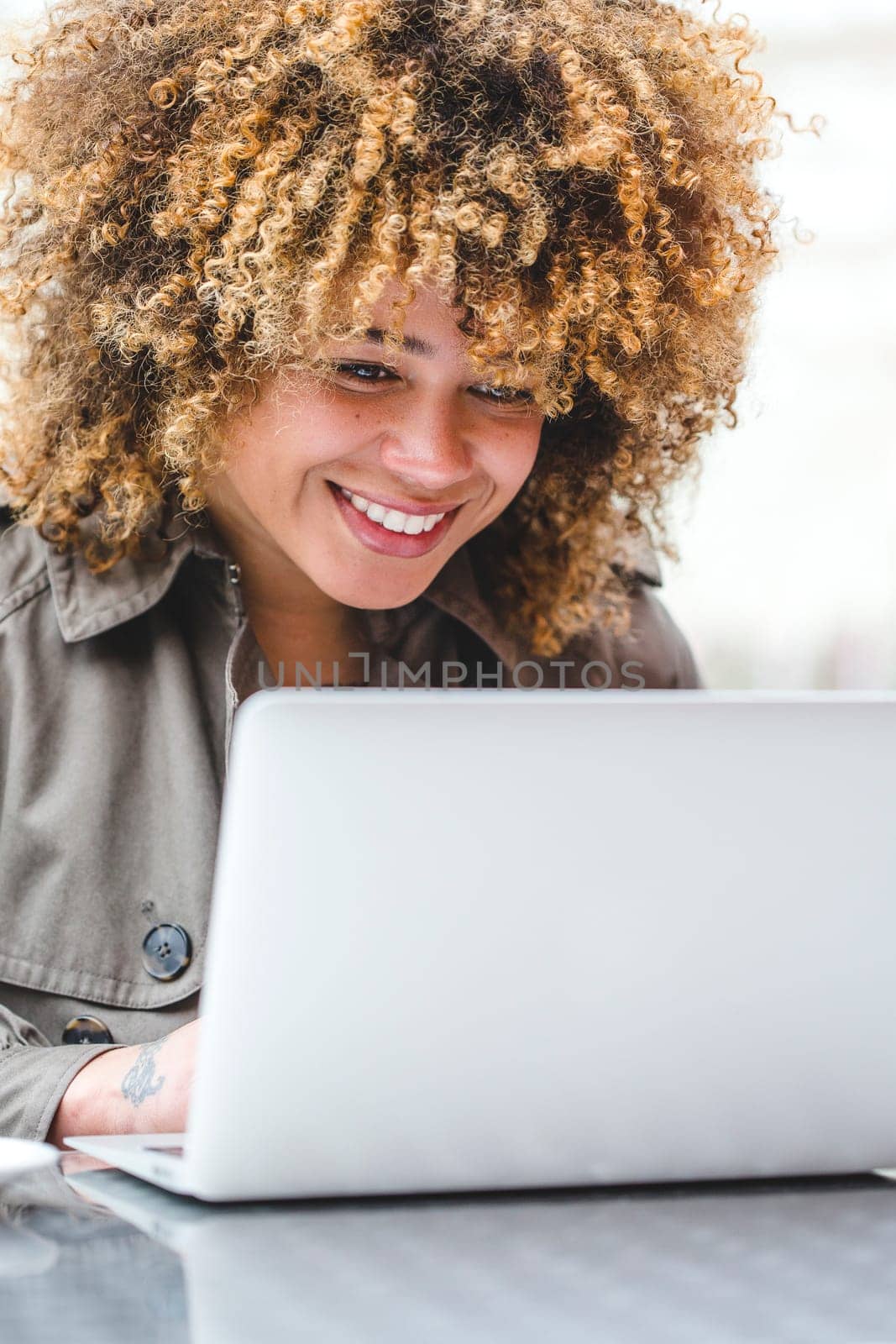 Woman sitting at a table using her laptop to video chat. She is smiling and looking at the screen.