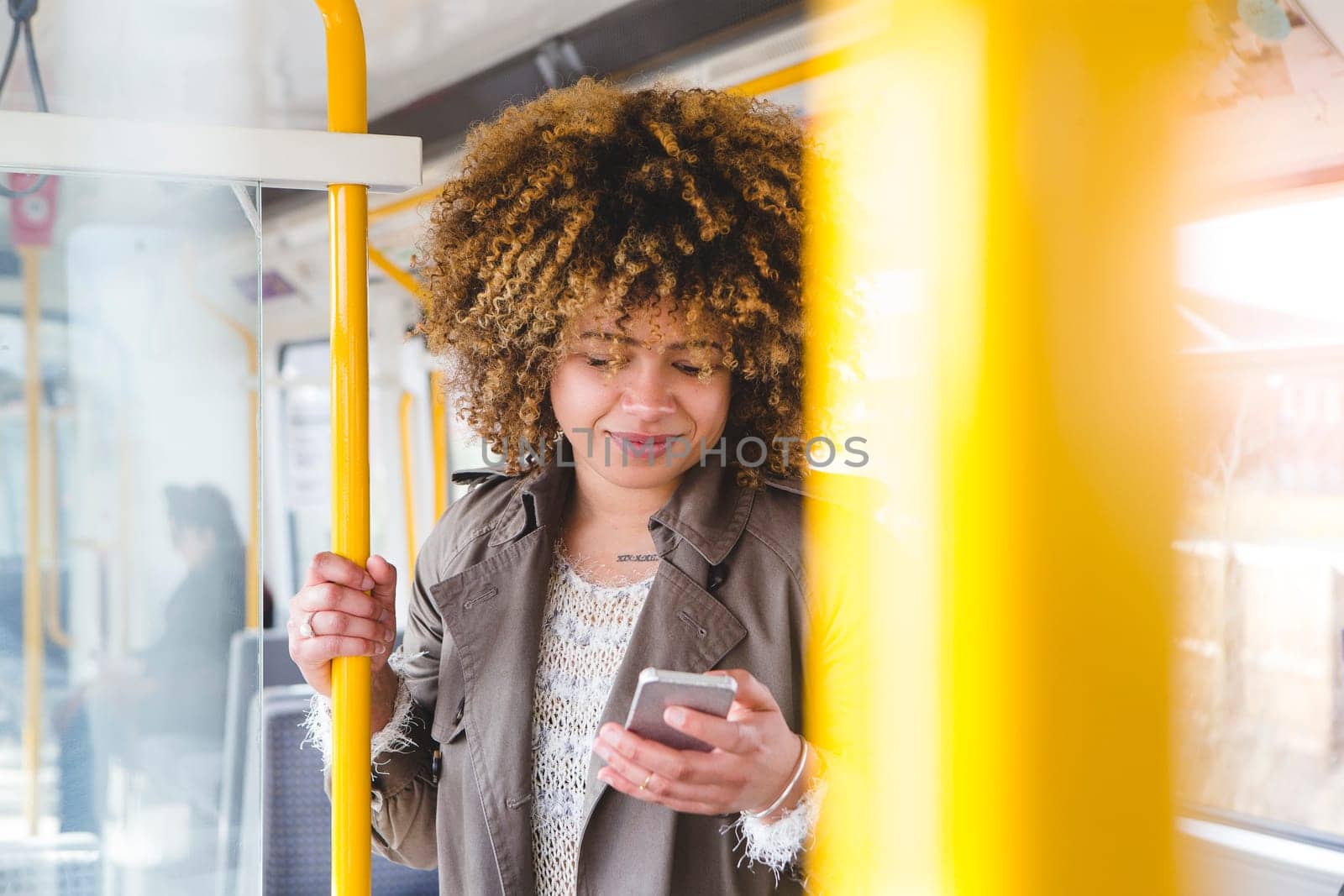 Woman using a smart phone on a train. She is holding on to the handrail with her other hand.
