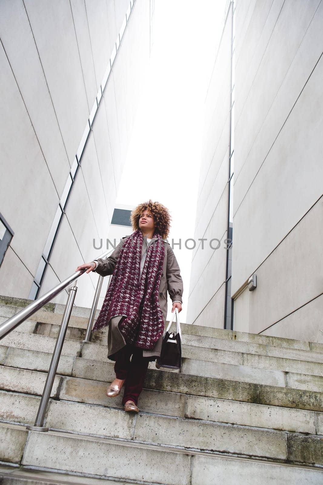 Woman walking down a staircase in the city. She looks as though she has just finished work and has her bag in hand.