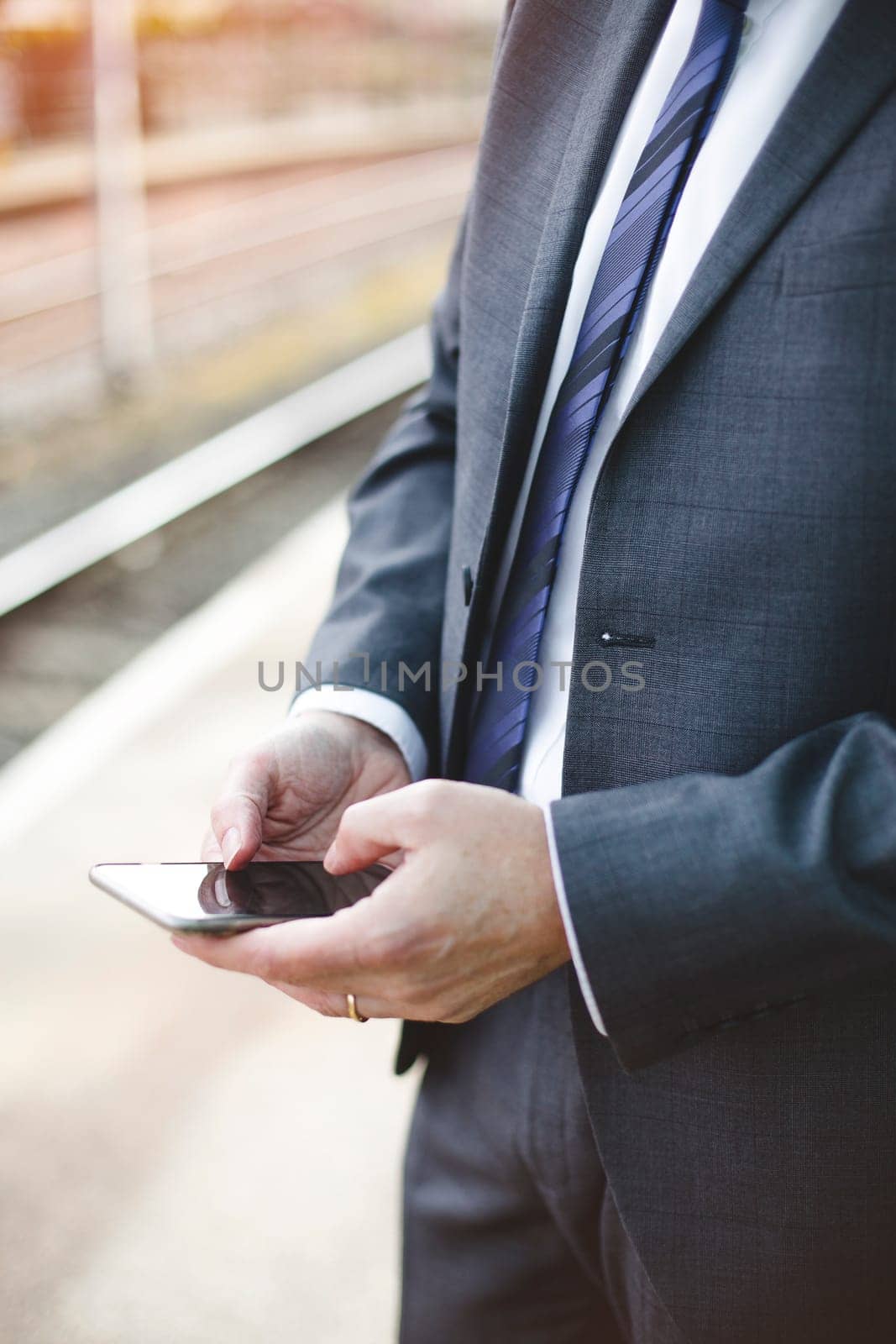 Man in a formal business suit using a smartphone outdoors. Only his torso is in the shot.