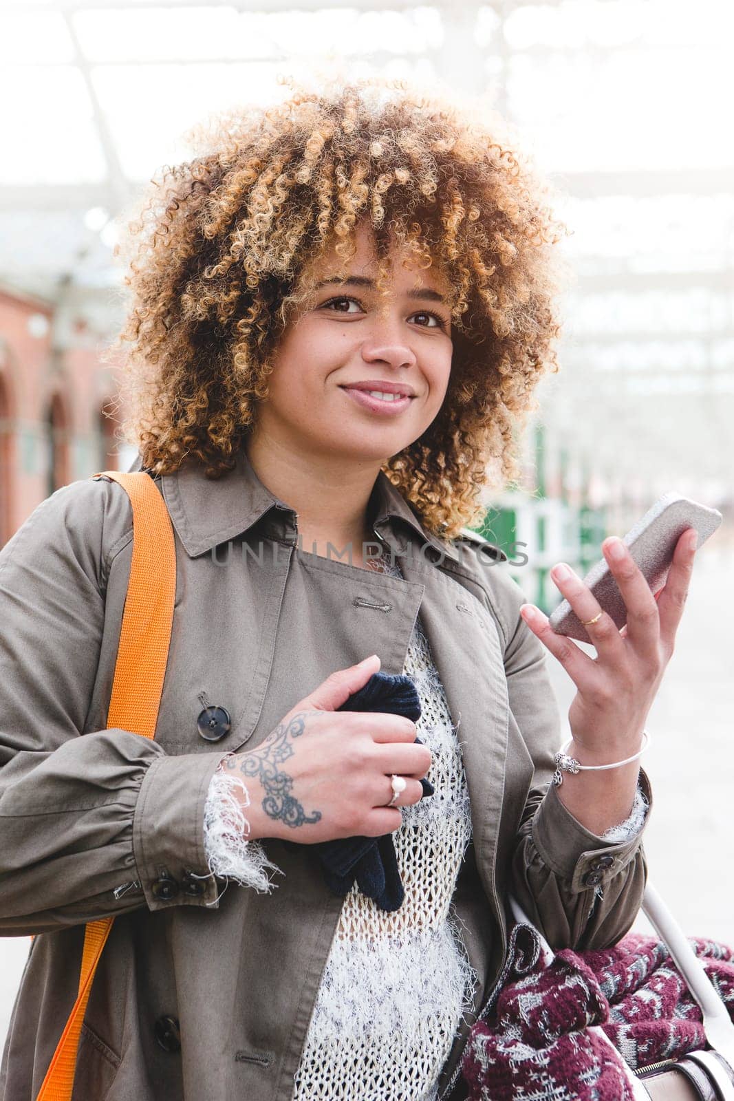 Woman waiting at the train station for her train. She is using her smart phone to check the times.