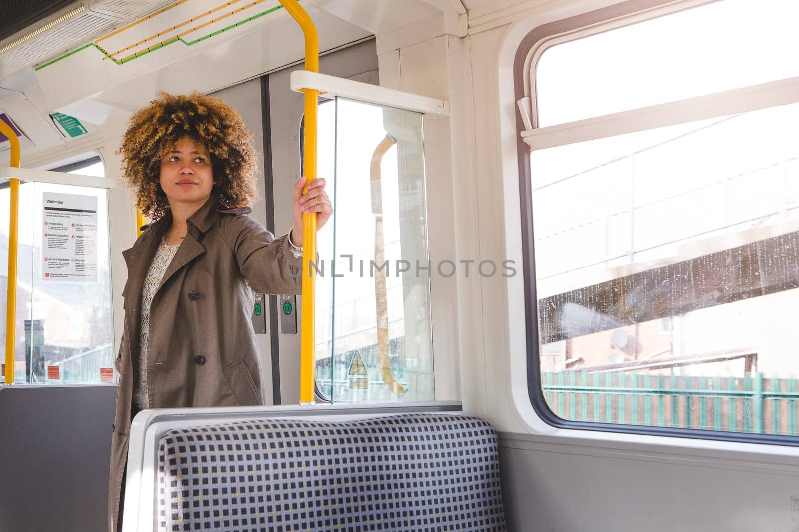 Woman commuting to work on a train. She is standing and holding on to the handle while looking out the window.