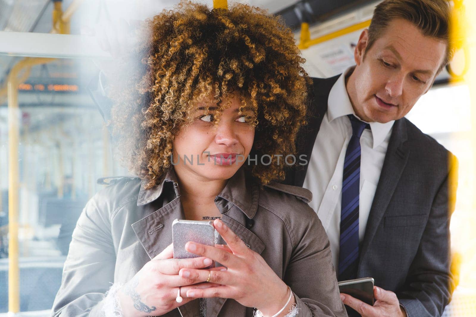 Man looking over a womans shoulder on the train at her phone screen.