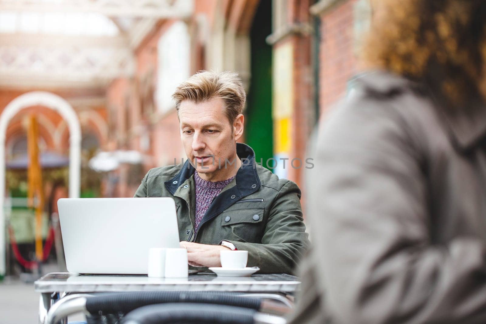 Man using a laptop at a cafe. He is sat at a table outside with a coffee.