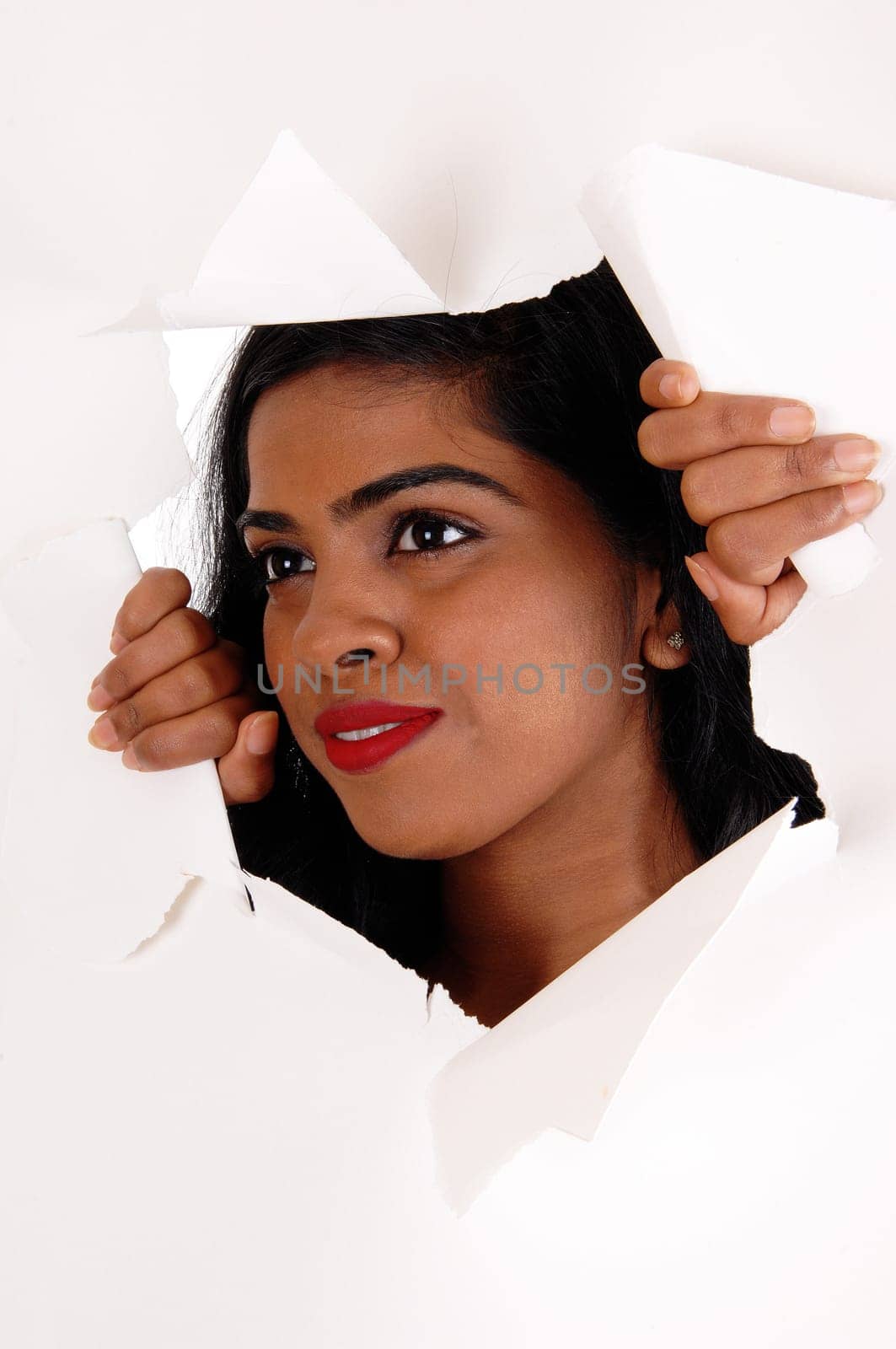 A pretty Indian woman with black hair looking trough a hole is a paper.with red lips, isolated for white background..