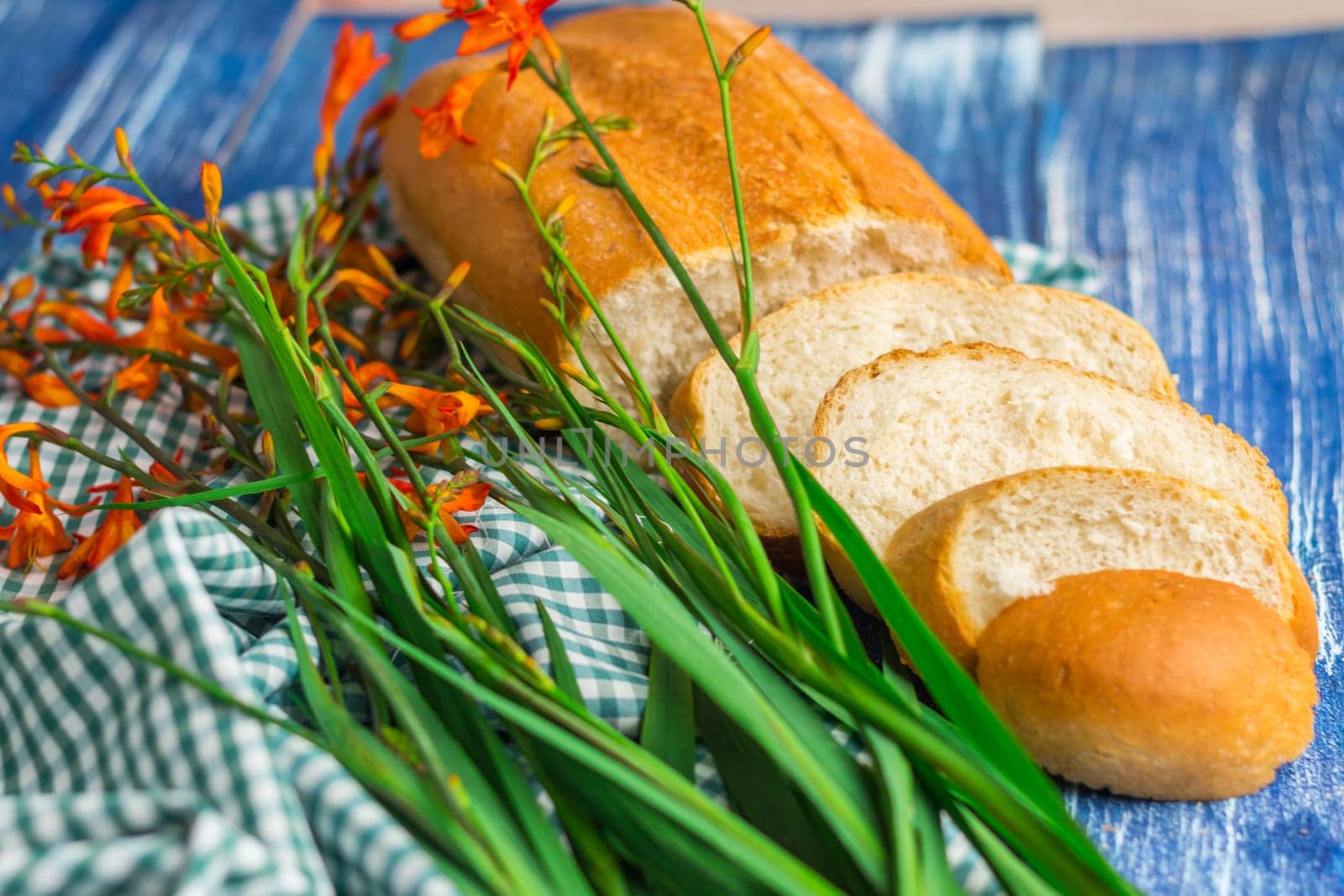 Fresh bread and flowers on blue wooden background and green fabric