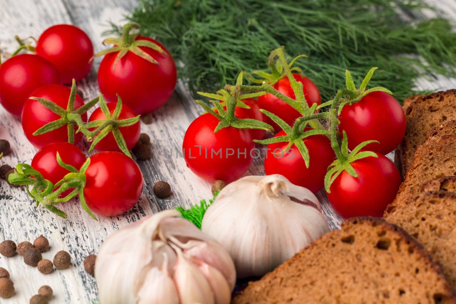 Still life on wooden background: tomatoes, black bread, garlic, fennel, bayberry pepper