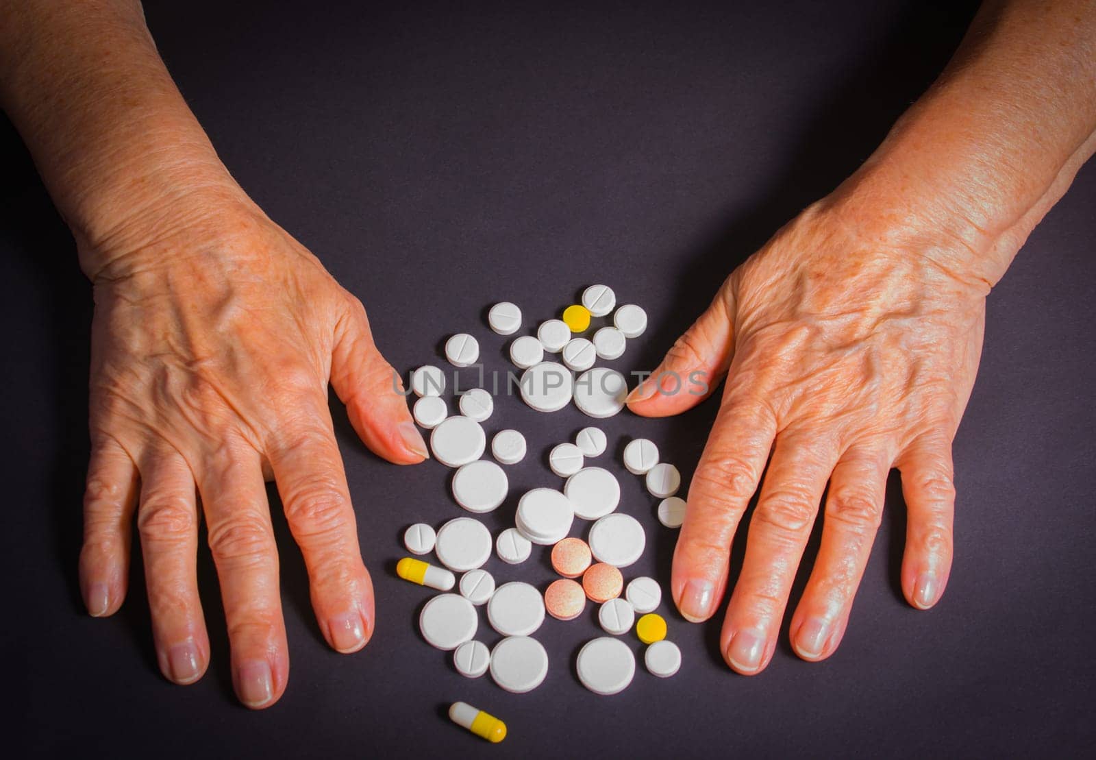The old female hands with pills on black background