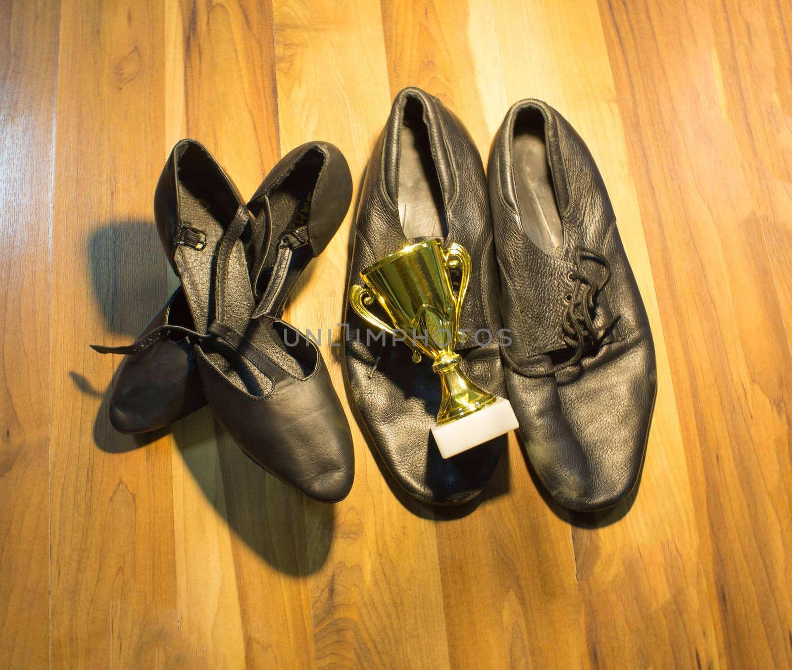 The black dance shoes of the man and woman on wooden floor background and golden cup of winner