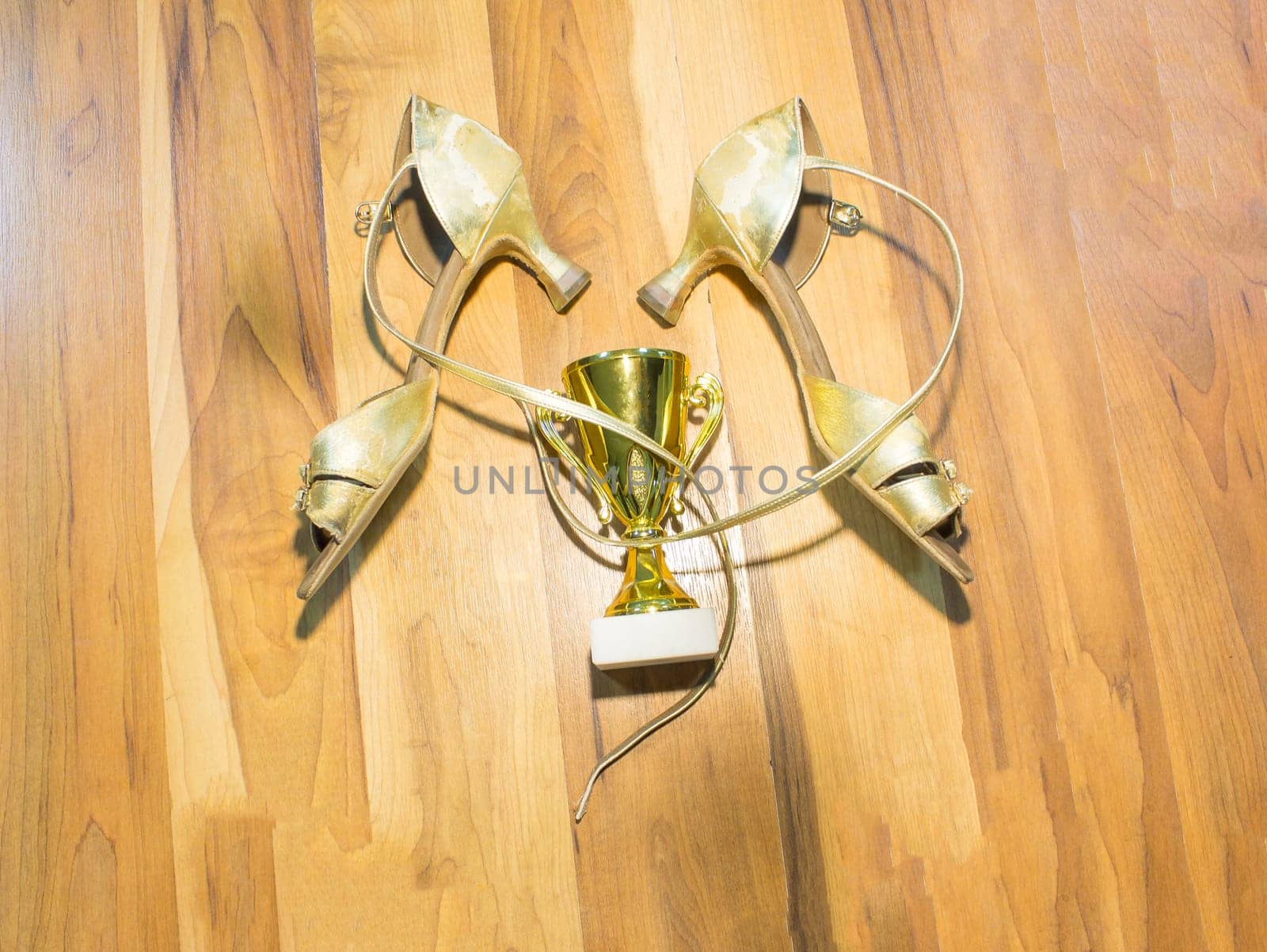 The old latin dance shoes on wooden floor background and golden cup of winner