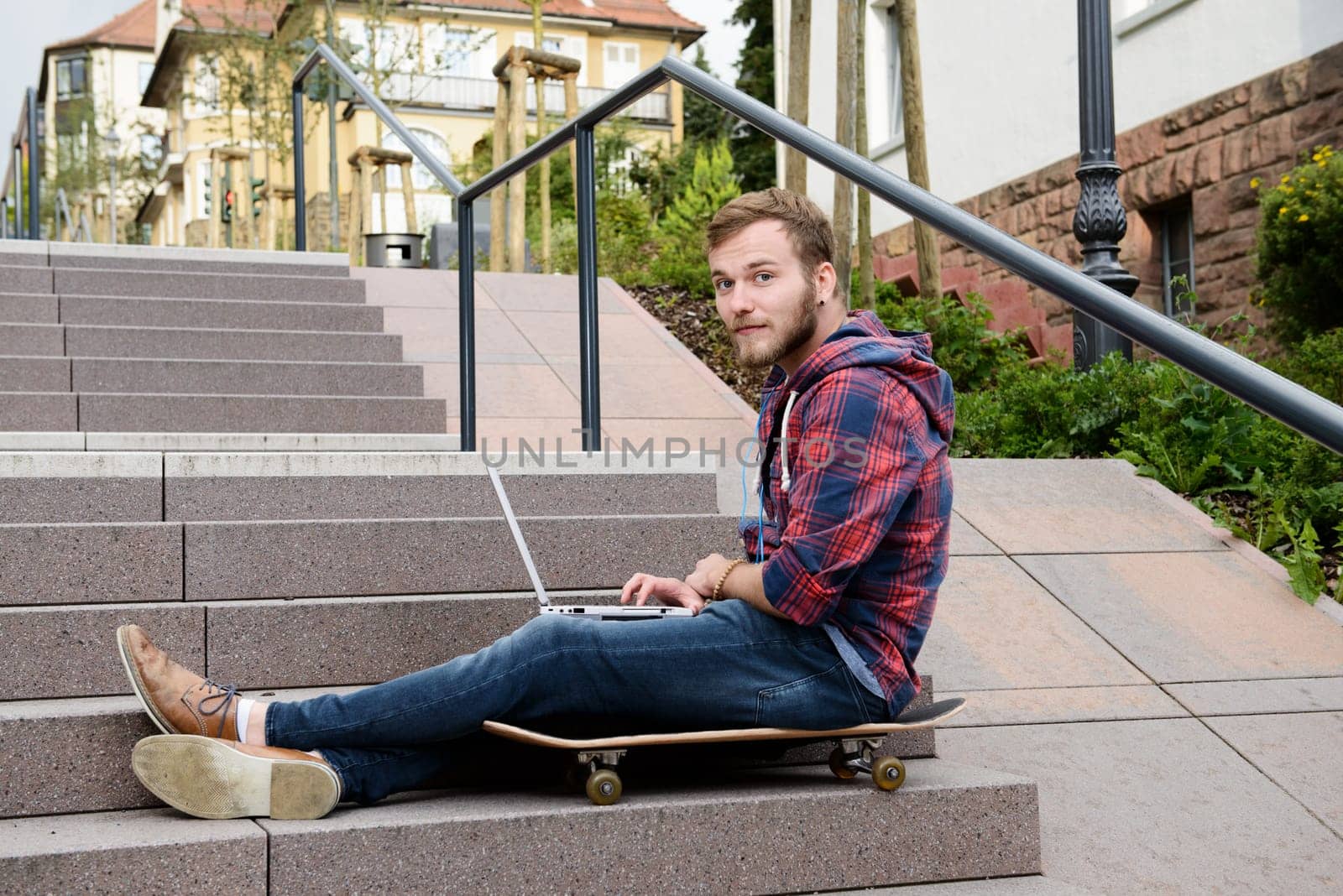 young man in checkered shirt sitting on stairs and using laptop