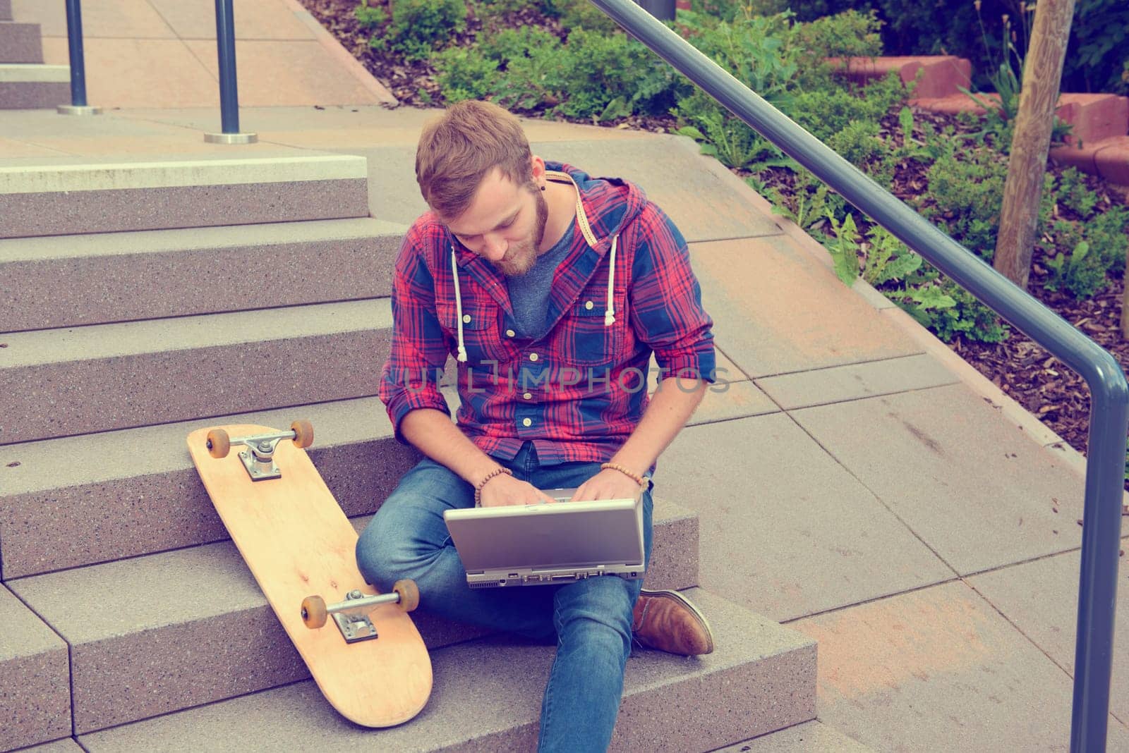 young man in checkered shirt sitting on stairs and using laptop