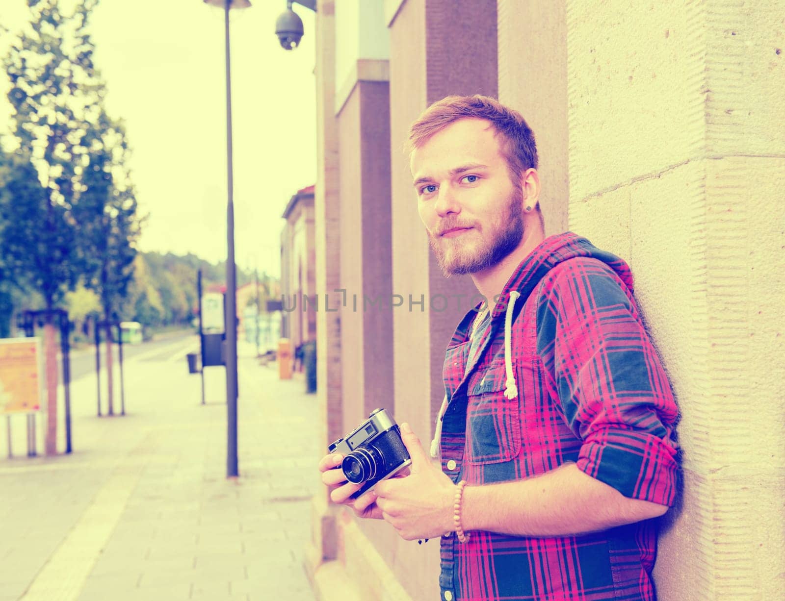 young bearded man with old camera standing in front of city background