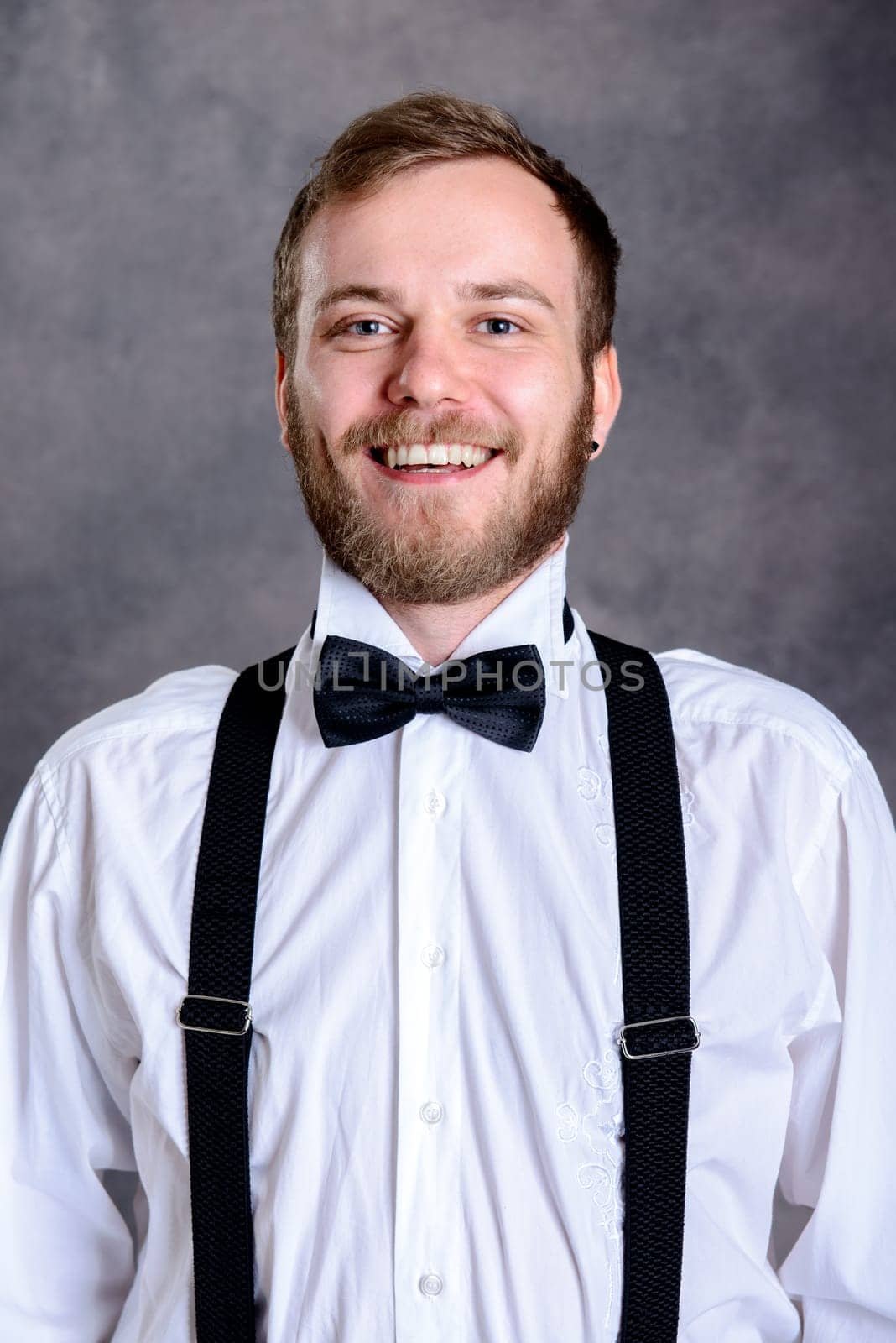young bearded man in white shirt and bow tie in front of gray background