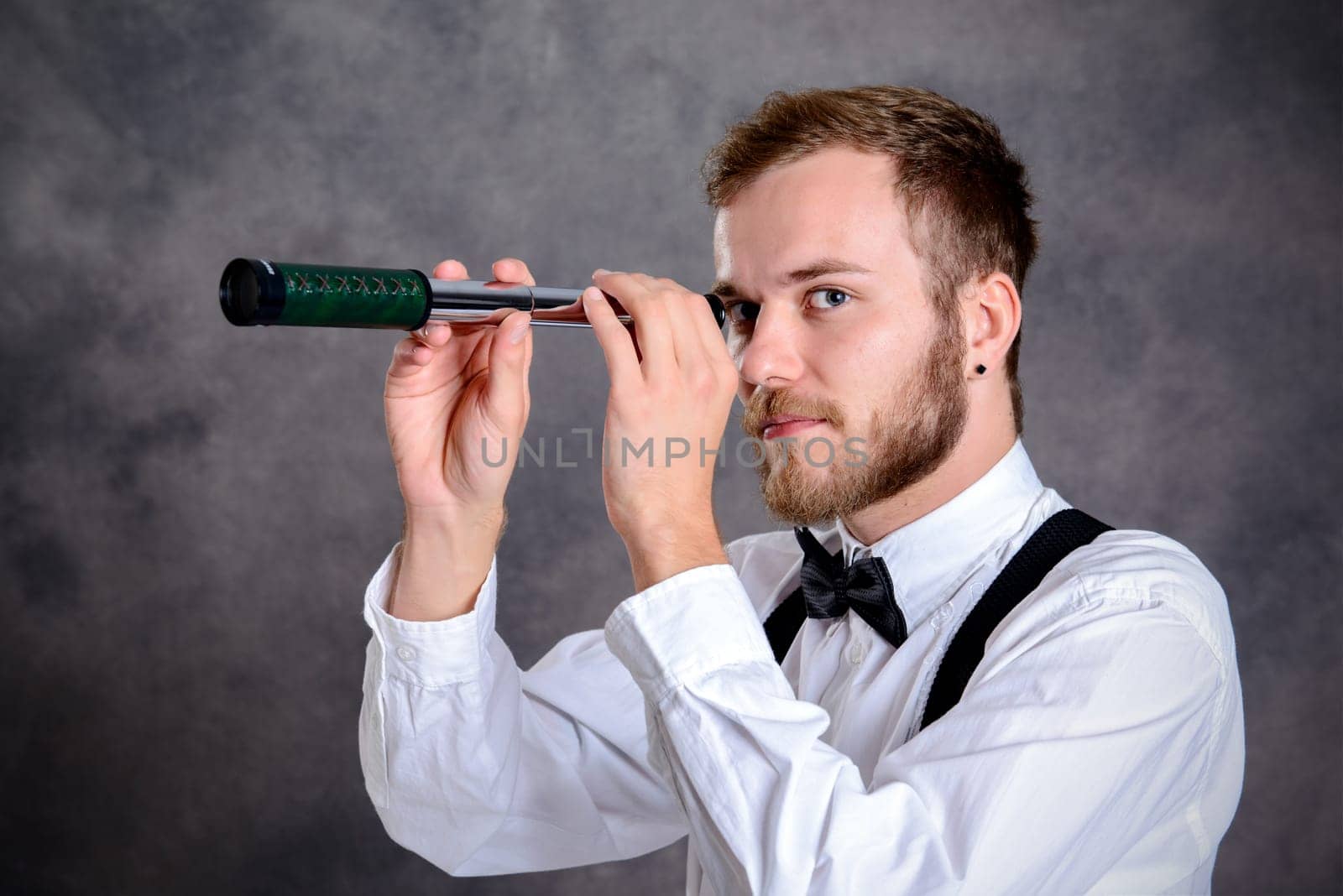 young bearded man in white shirt and bow tie looking through a telescope