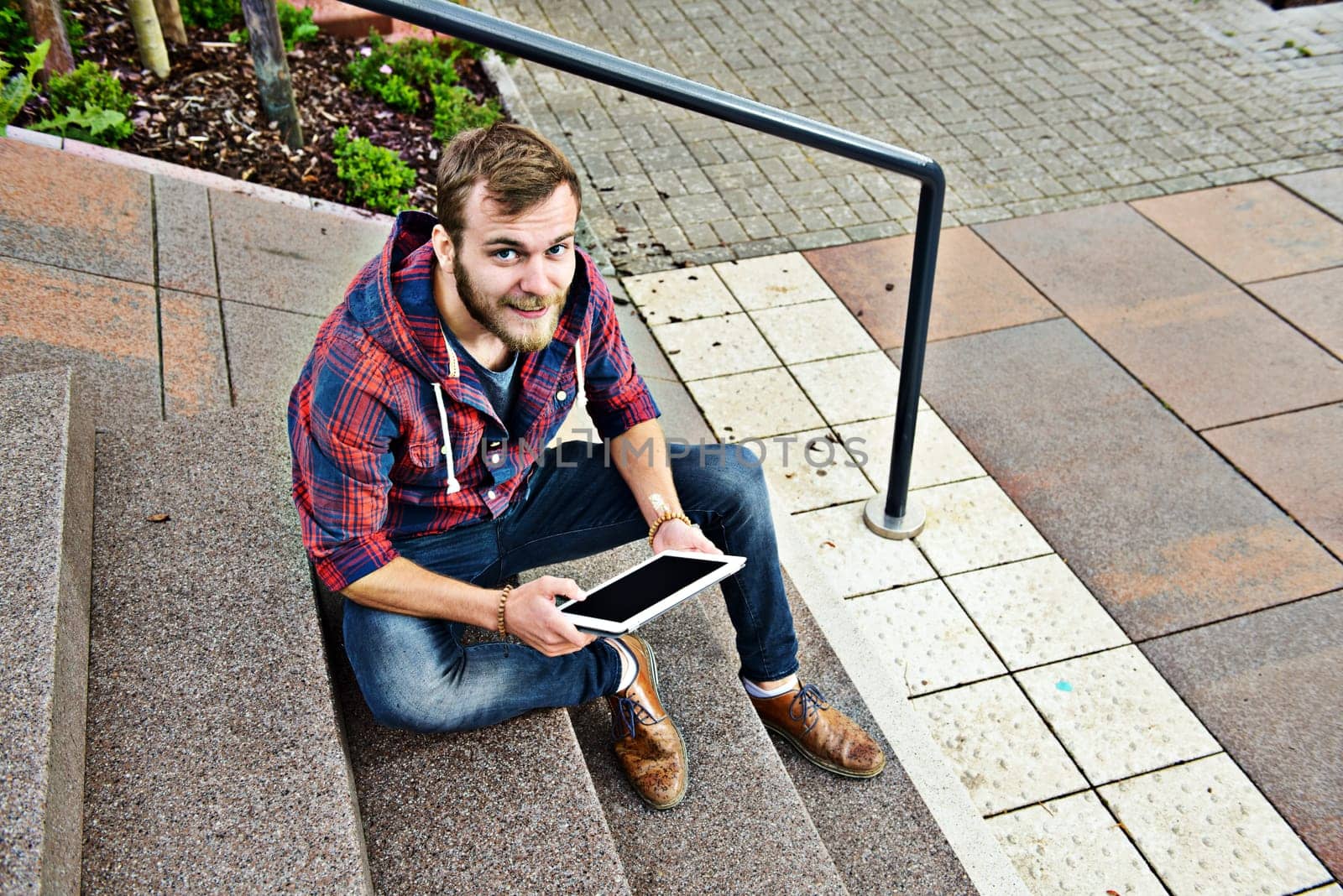 young man in checkered shirt sitting on stairs and using tablet PC