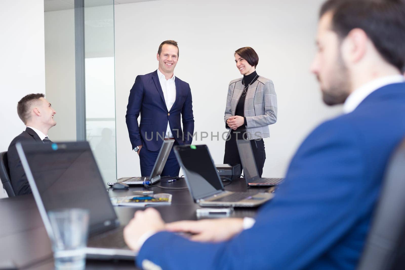 Successful team leader and business owner leading informal in-house business meeting. Businessman working on laptop in foreground. Business and entrepreneurship concept.