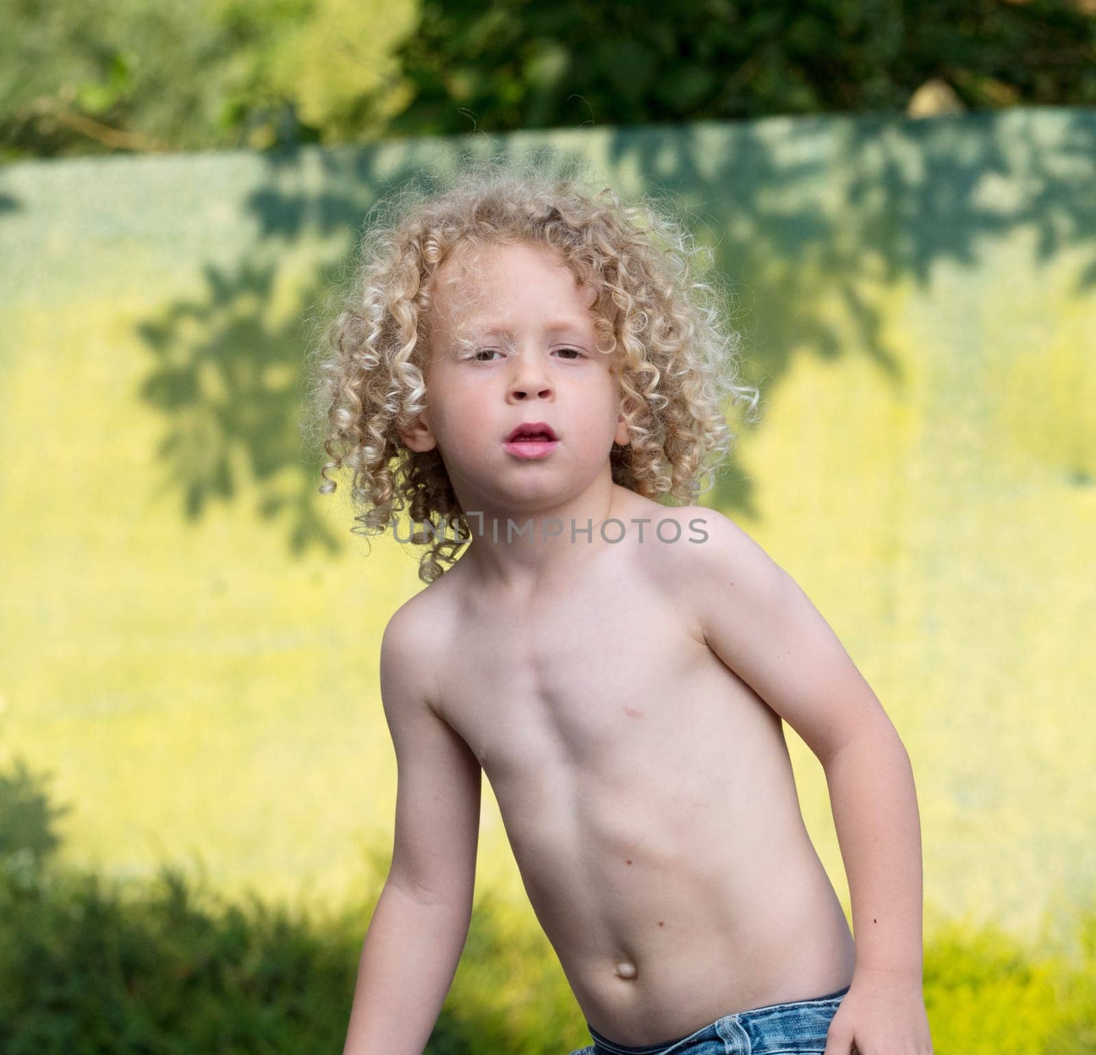 little blond boy shirtless playing in the garden