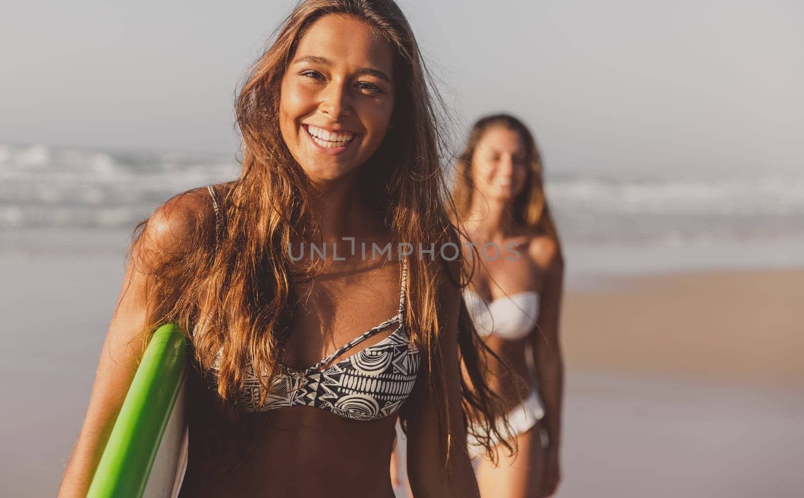 Best friends enjoying the summer, walking on the beach with a surfboard
