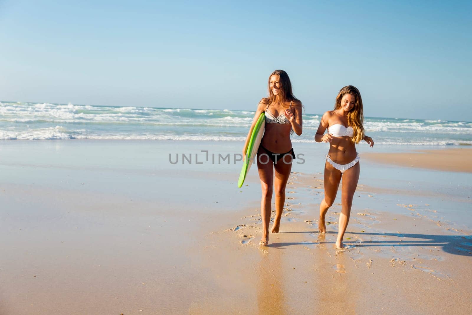 Best friends enjoying the summer, running on the beach with a surfboard