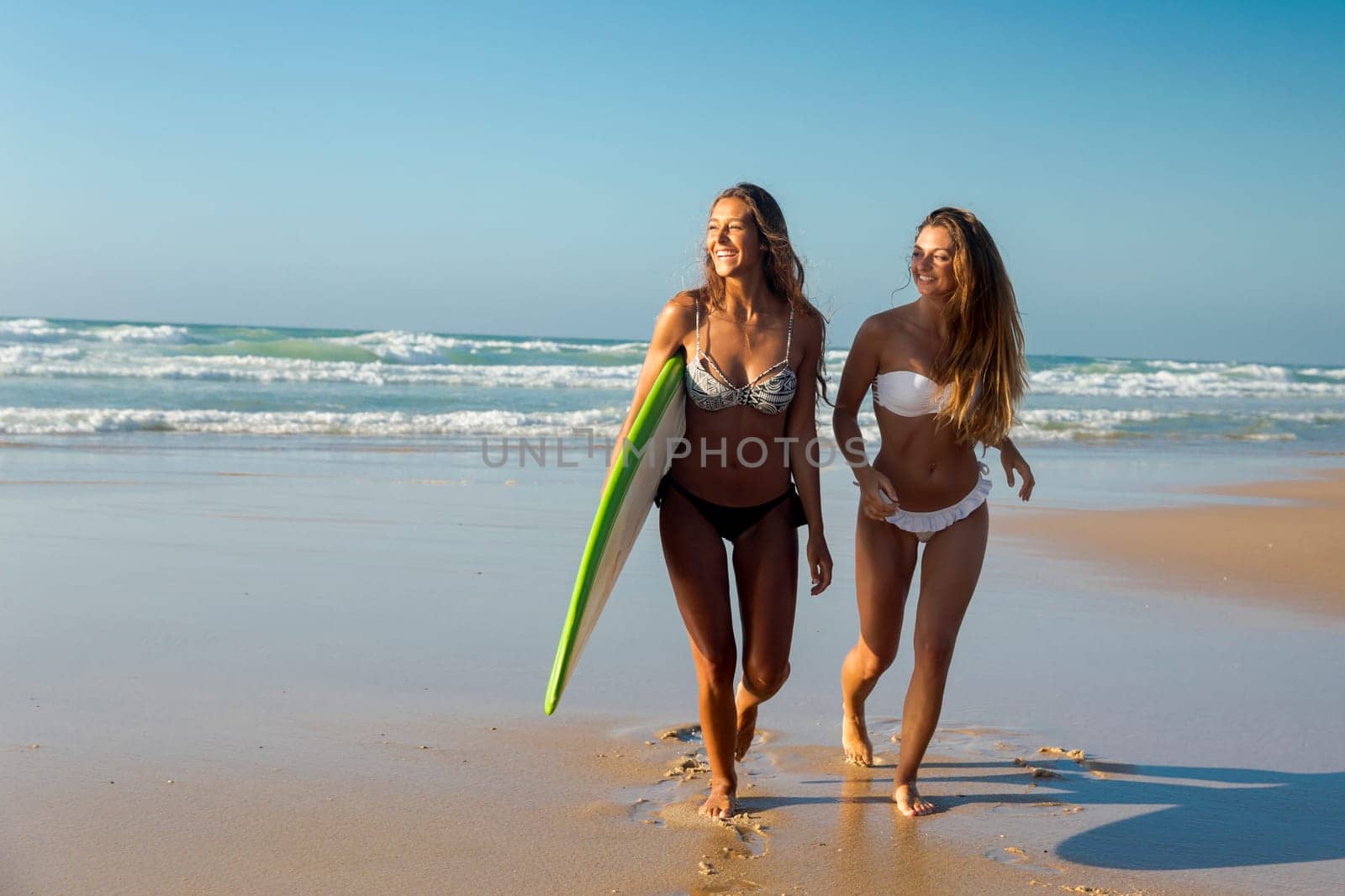 Best friends enjoying the summer, running on the beach with a surfboard
