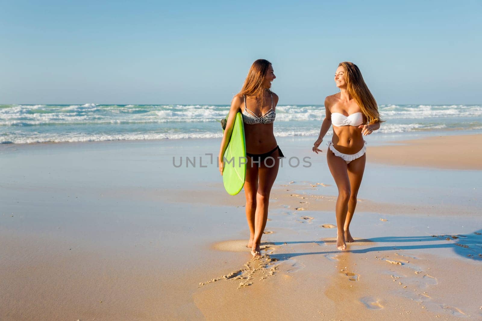 Best friends enjoying the summer, running on the beach with a surfboard