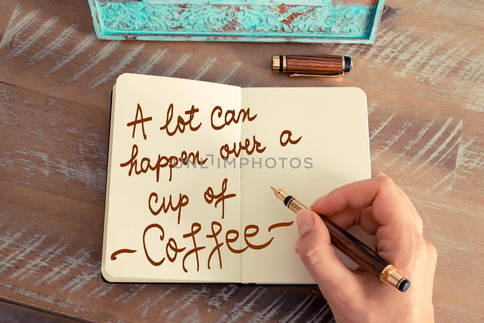 Handwritten text A Lot Can Happen Over A Cup Of Coffee as business image. Retro effect and toned image of a woman hand writing a note with fountain pen on a notebook.