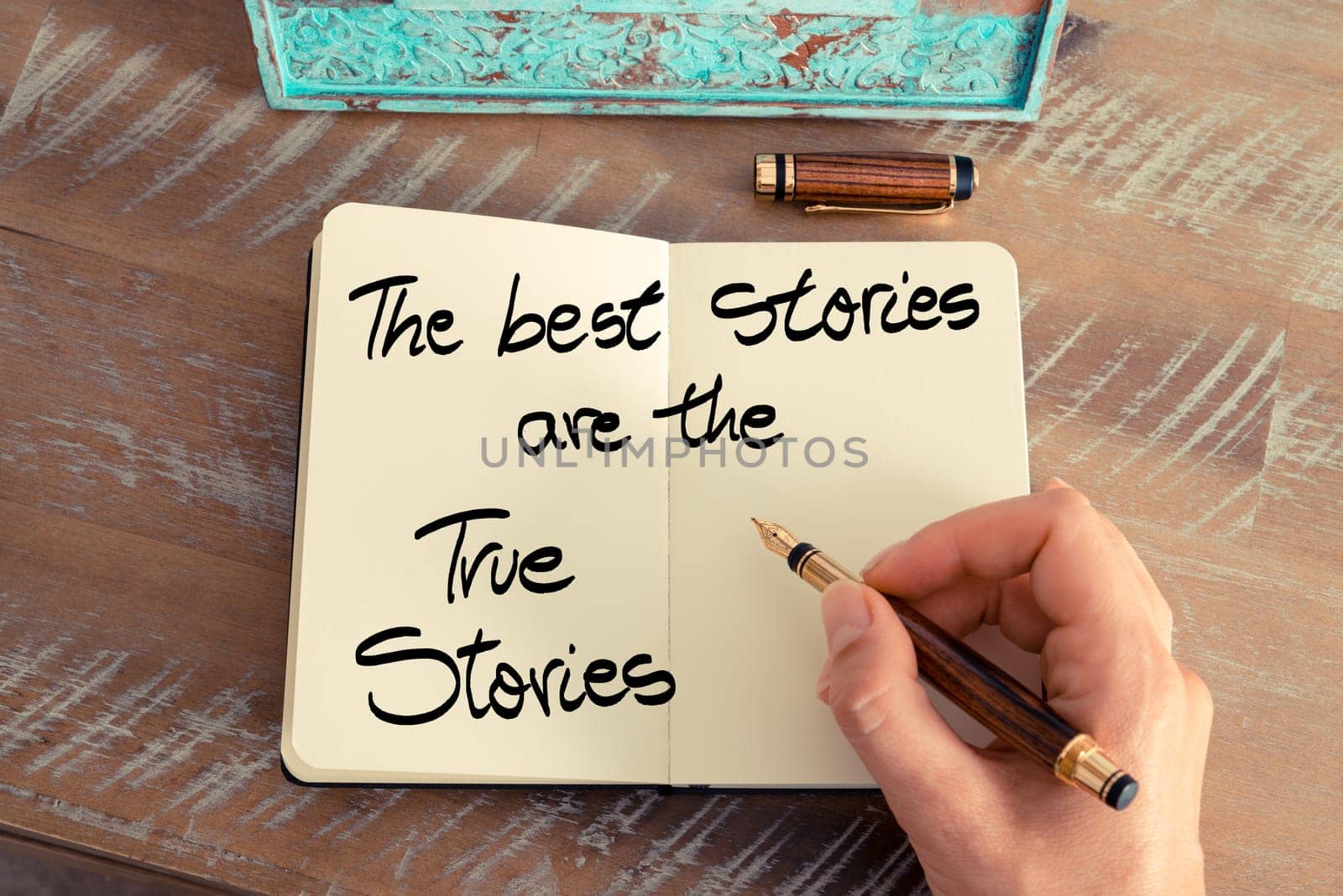 Handwritten text The Best Stories Are The True Stories as business image. Retro effect and toned image of a woman hand writing a note with fountain pen on a notebook.
