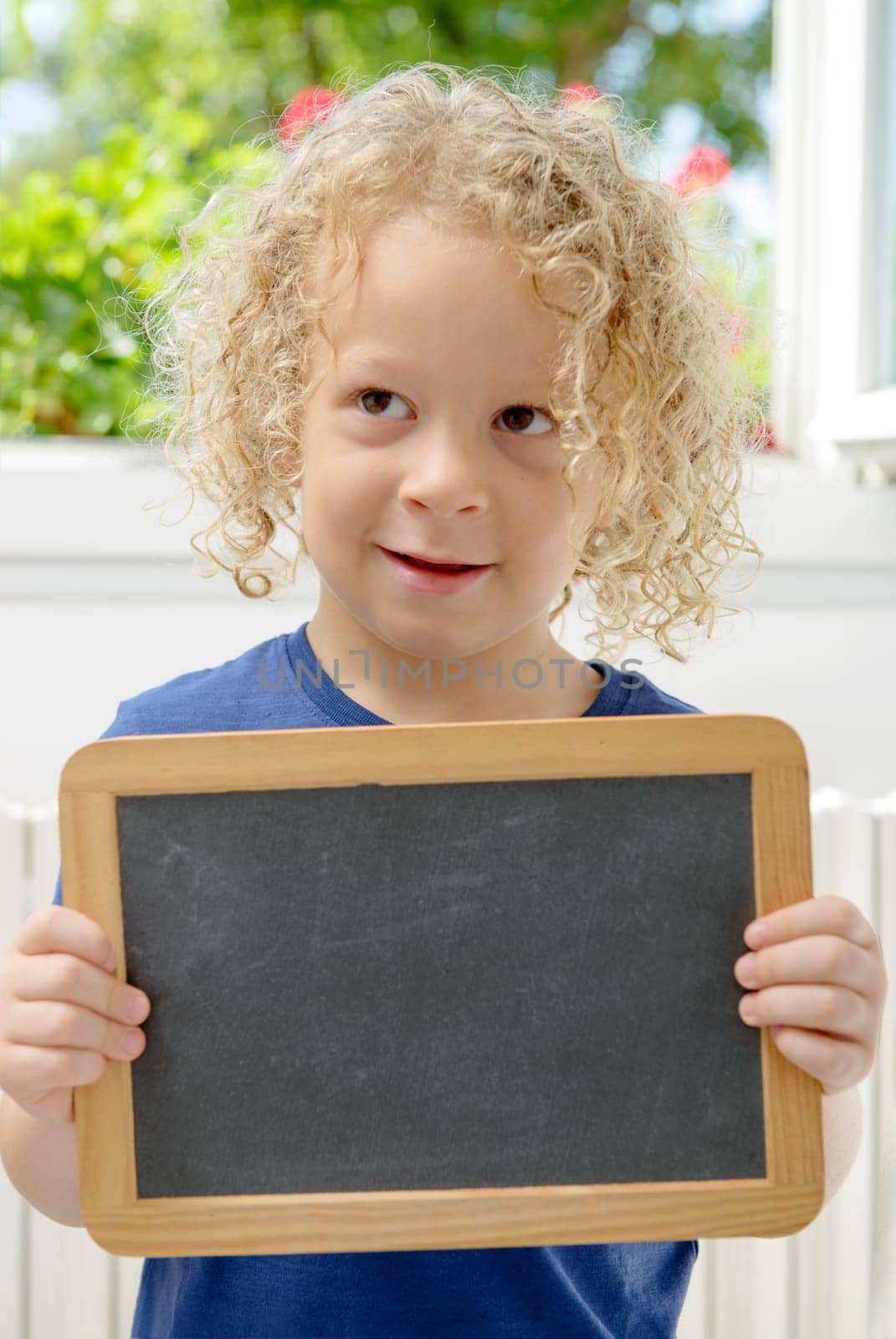 a blond and curly boy holding a chalkboard