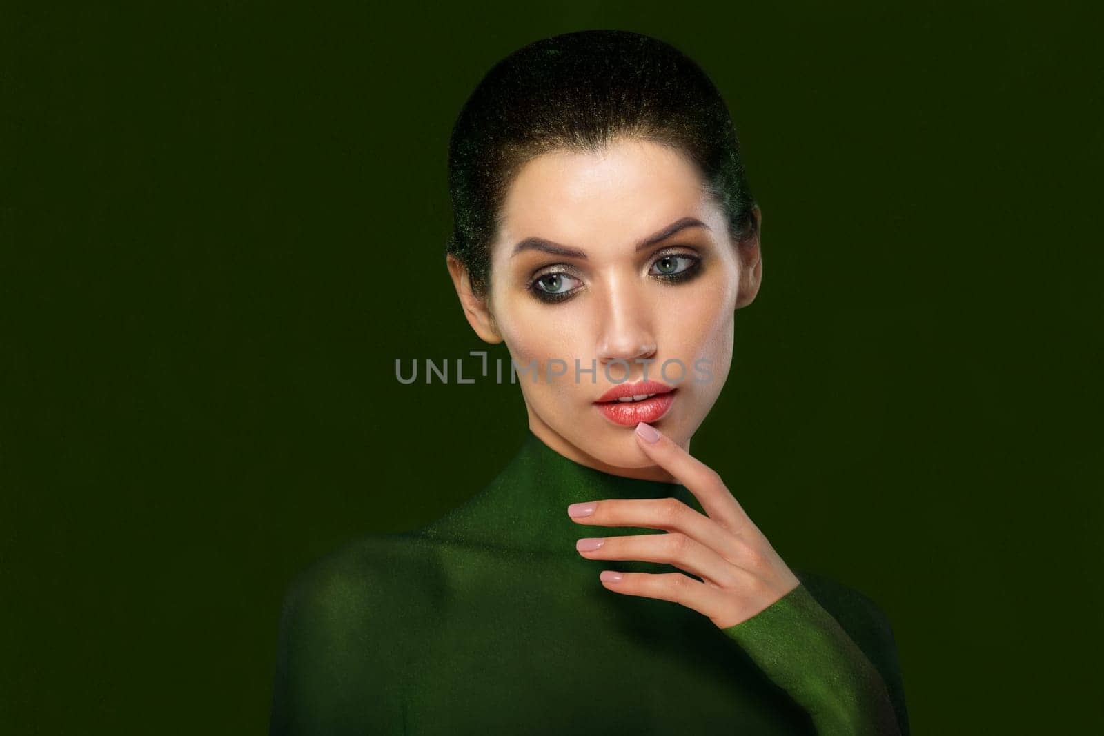 Portrait of a beautiful woman on a green background. Close-up face. think. Thumb near the lips.